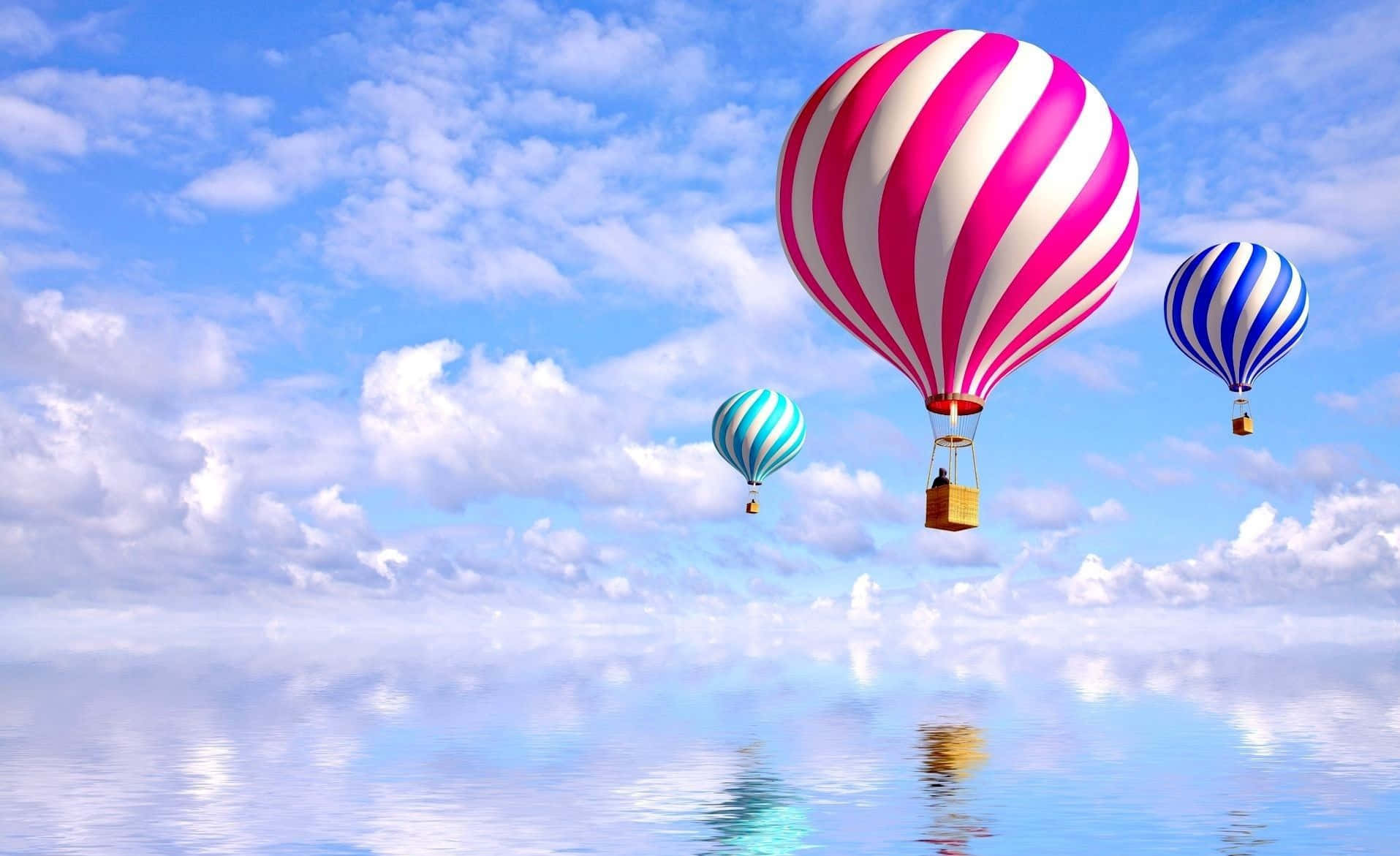 Hot Air Balloon 桌布 壁紙 — 三個色彩繽紛的條紋熱氣球在晴朗藍天和 fluffy 雲朵下，平靜地漂浮在平靜的反射湖面上。