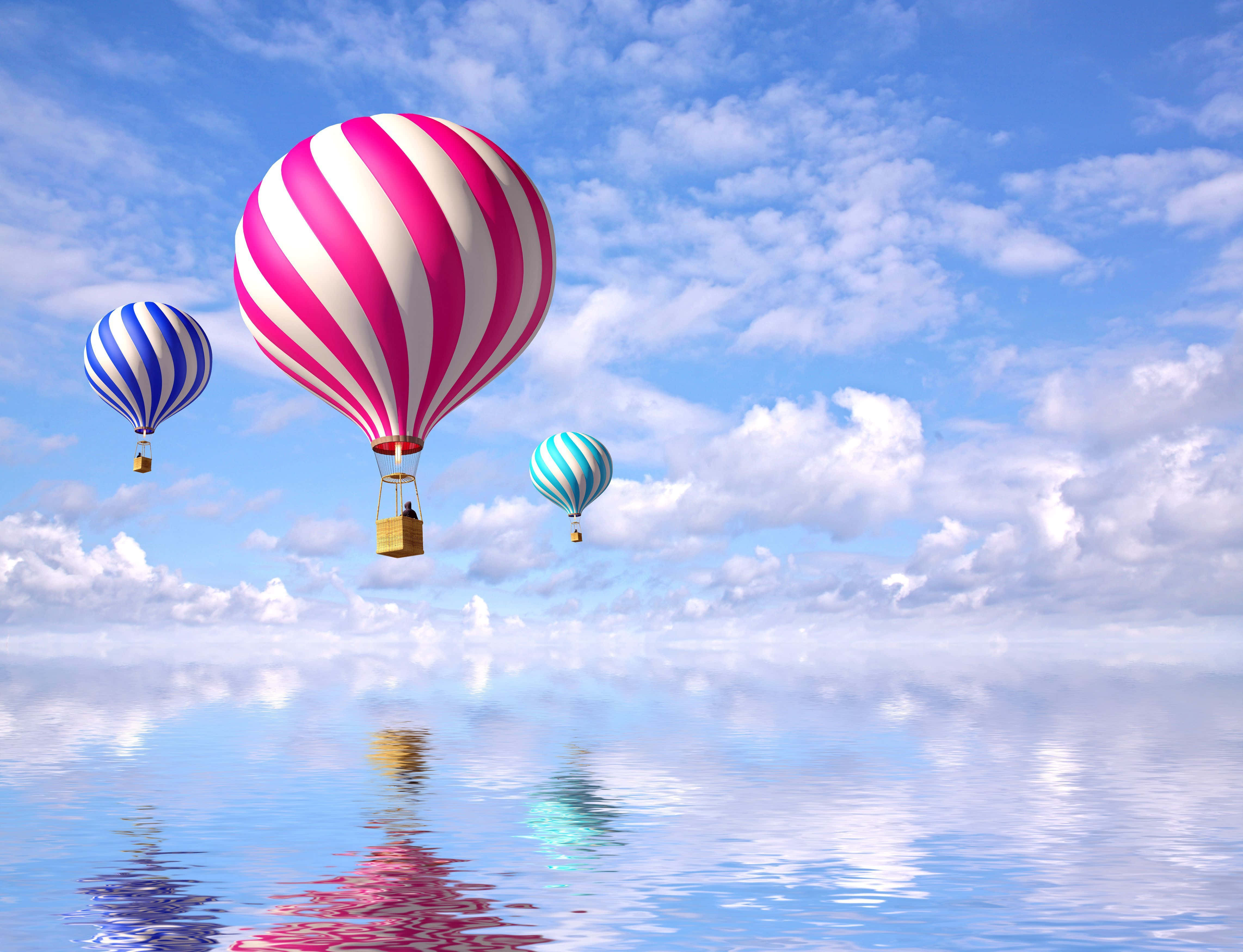 Balloon 桌布 壁紙 — 三個色彩繽紛的條紋熱氣球漂浮在平靜的反射表面上，下方是明亮的藍天和蓬鬆的雲朵。