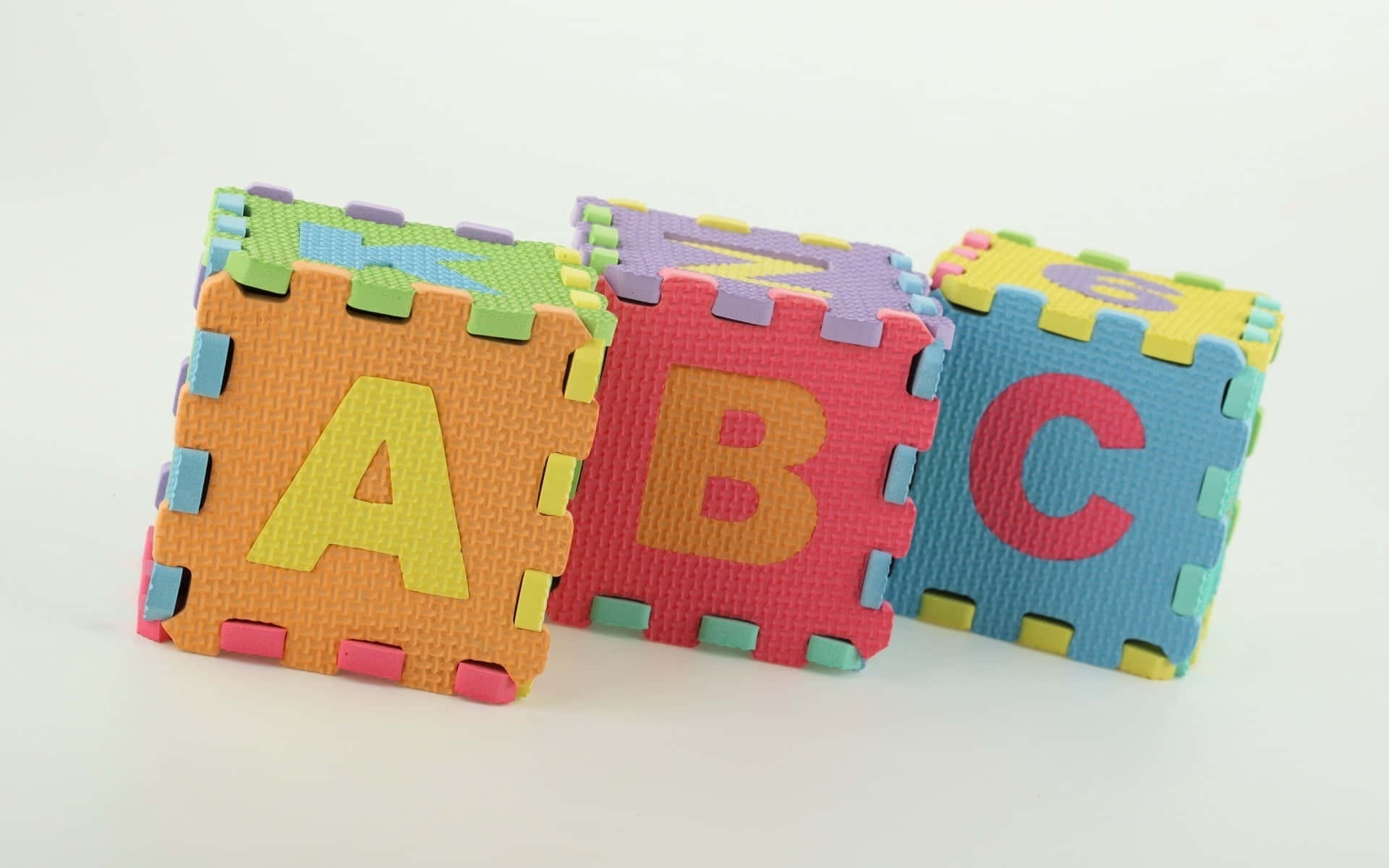 Educational Games 桌布 壁紙 — 三個色彩繽紛的泡棉字母積木拼出ABC，放在純白表面上。