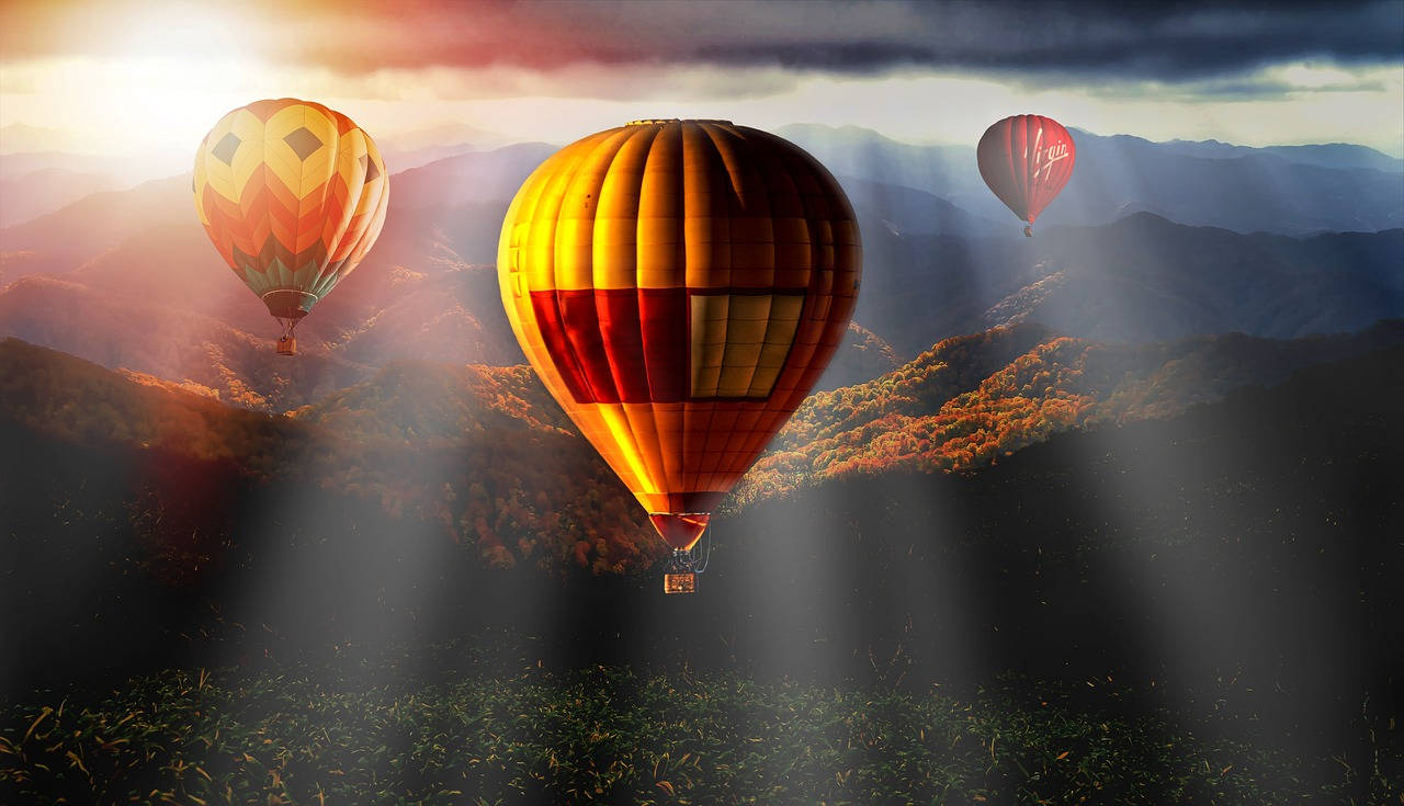Hot Air Balloon 桌布 壁紙 — 三個色彩繽紛的熱氣球在沐浴著金色日出光芒的山區地形上空飄移，伴隨著戲劇性的雲層。