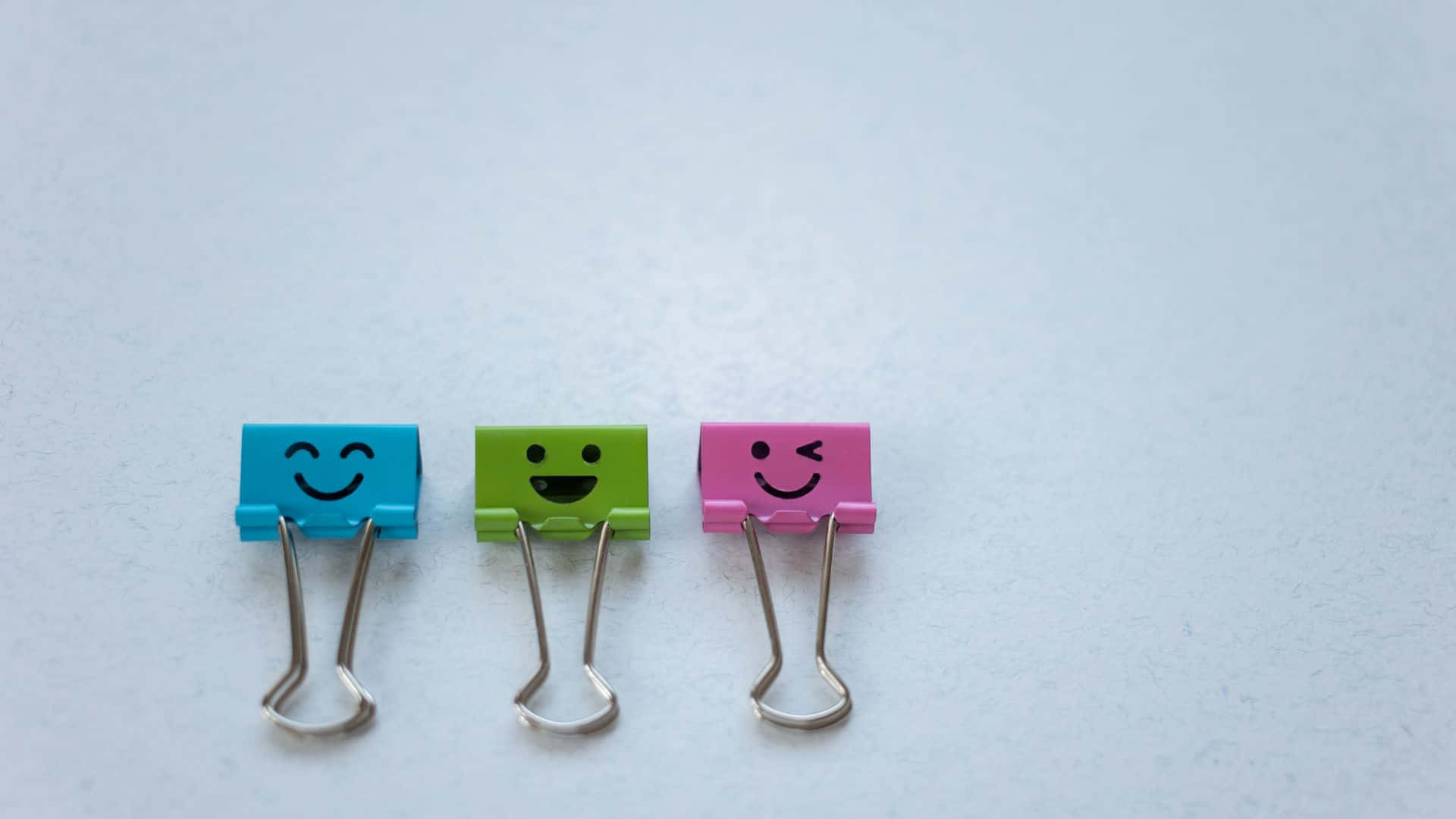 Smiley 桌布 壁紙 — 三個色彩繽紛的笑臉文件夾夾子並排放在純白色表面上。