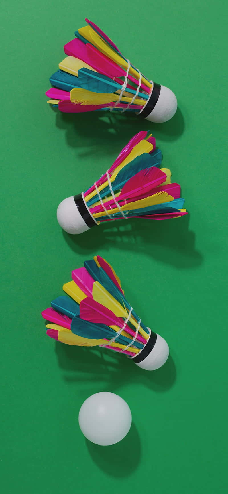 Android Badminton 桌布 壁紙 — 三個色彩繽紛的羽毛球和一個白色球對角排列在充滿活力的綠色表面上。