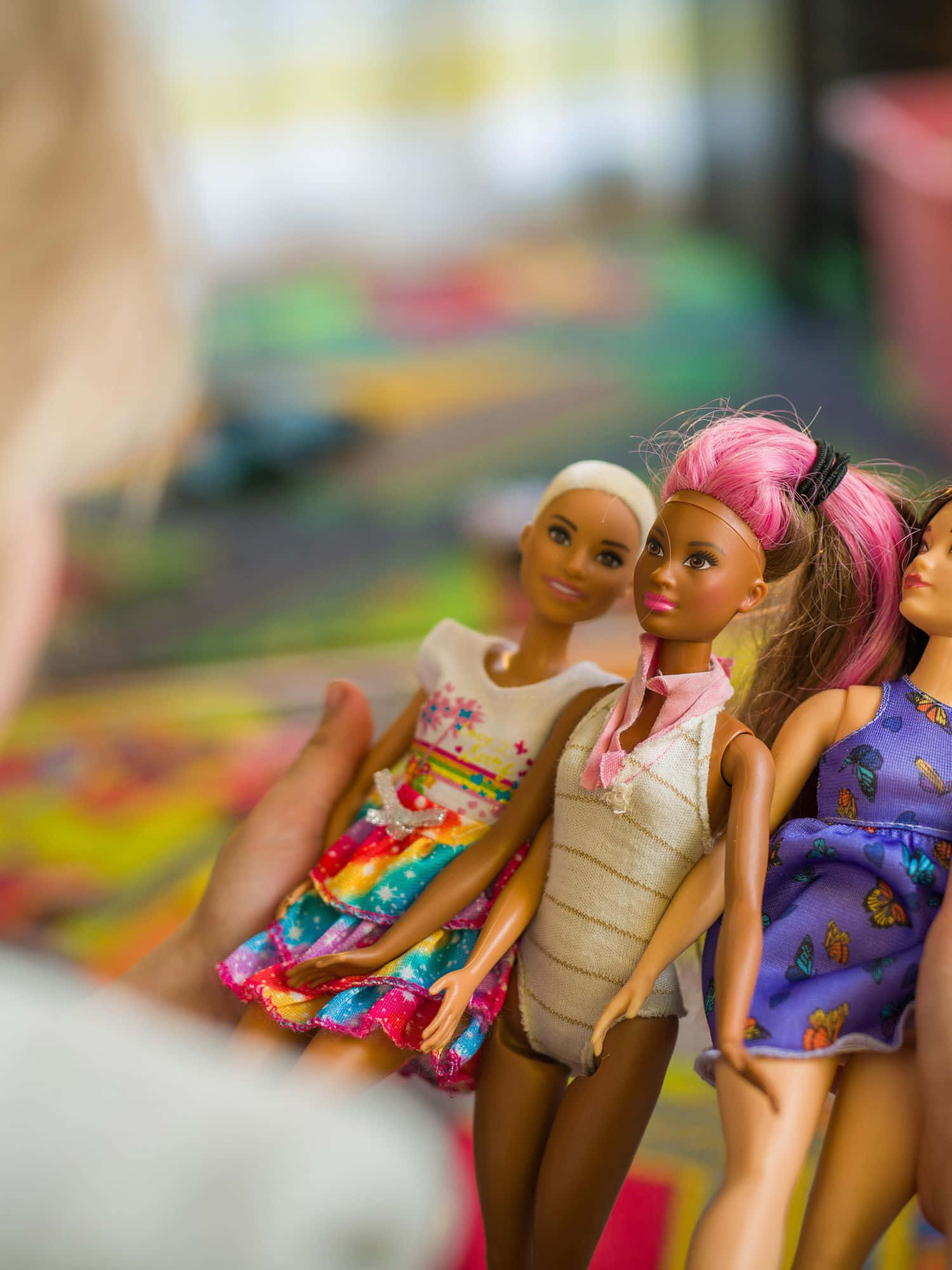 Doll 桌布 壁紙 — 三個色彩繽紛的芭比娃娃，各有不同的髮型和服裝，被輕輕握在一個孩子的手中，背景是模糊而充滿活力的。