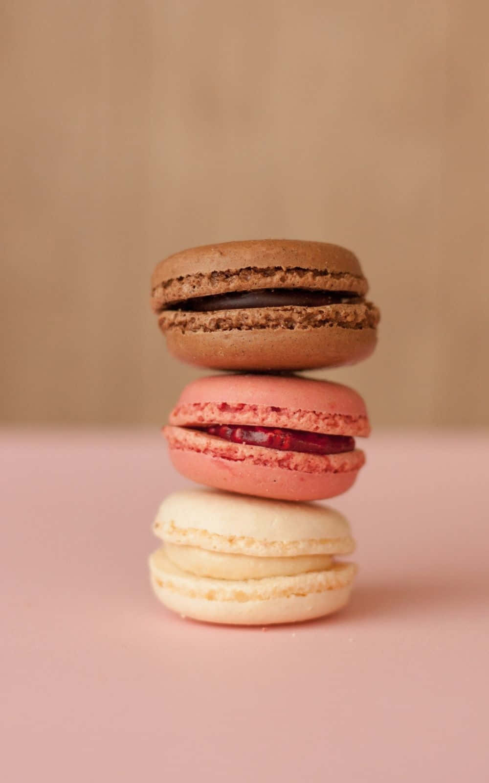 Food Photography 桌布 壁紙 — 三個色彩繽紛的馬卡龍垂直堆疊在柔軟的粉紅色表面上，背景是溫暖的米色。