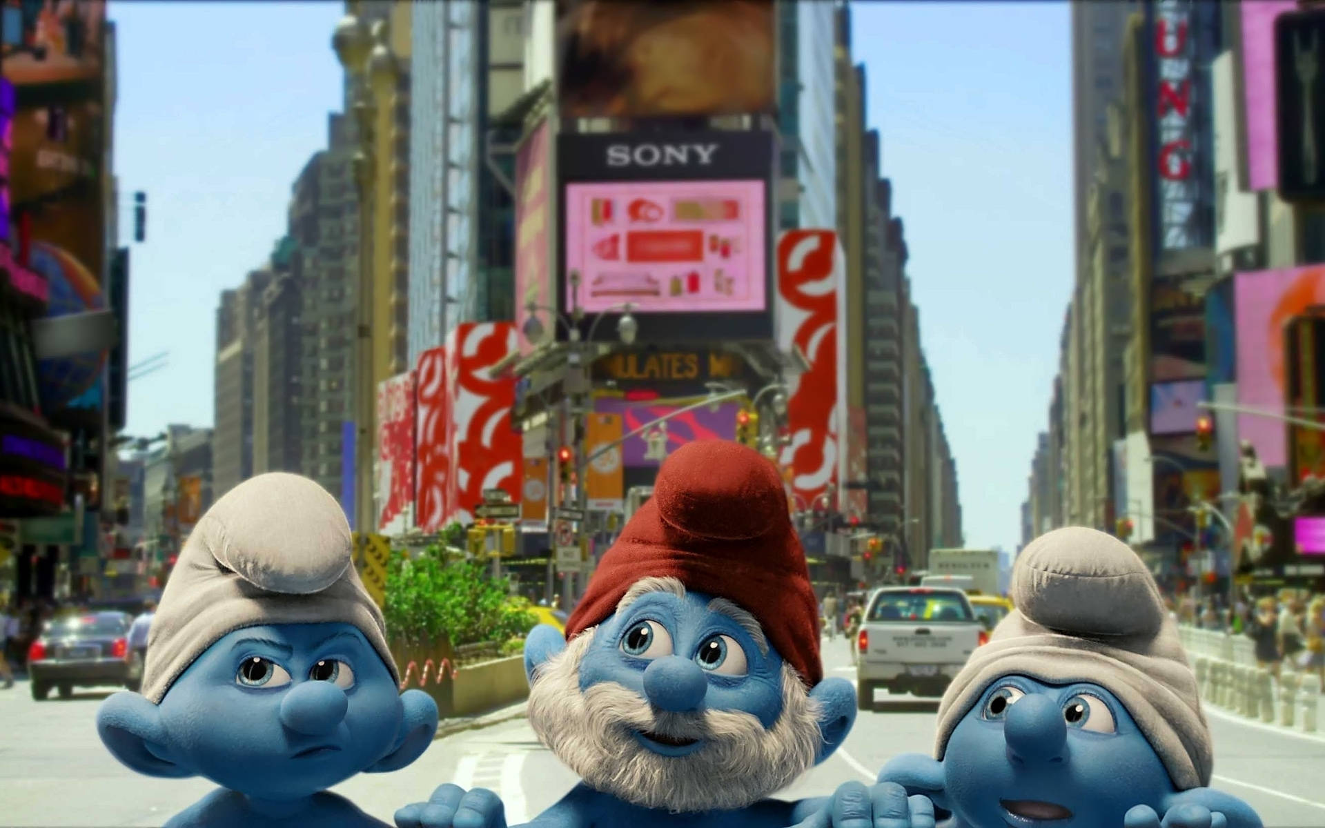 Smurfs 桌布 壁紙 — 三個藍皮膚、戴白帽的藍色小精靈站在繁華的時代廣場街道上，周圍是高樓大廈和明亮的廣告牌。