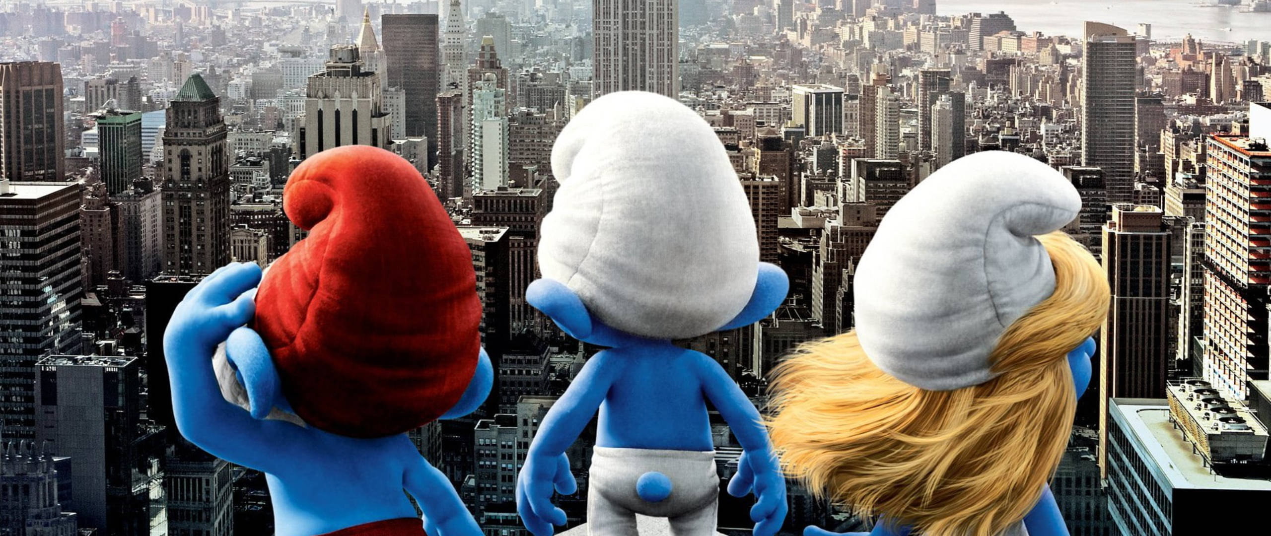 Smurfs 桌布 壁紙 — 三個藍色小精靈戴著紅色、白色和金色的帽子，從高處俯瞰廣闊的城市景觀。