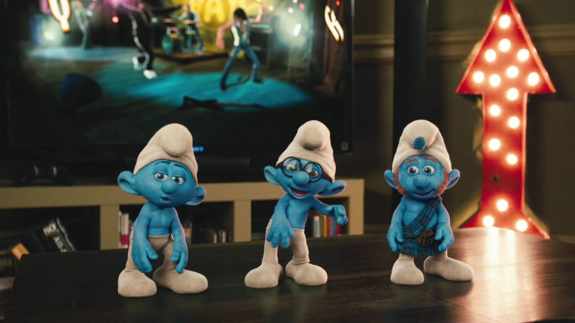 Smurfs 桌布 壁紙 — 三個藍色藍色小精靈公仔坐在一張深色桌子上看電視上的音樂會，旁邊有一個發光的紅色箭頭燈。
