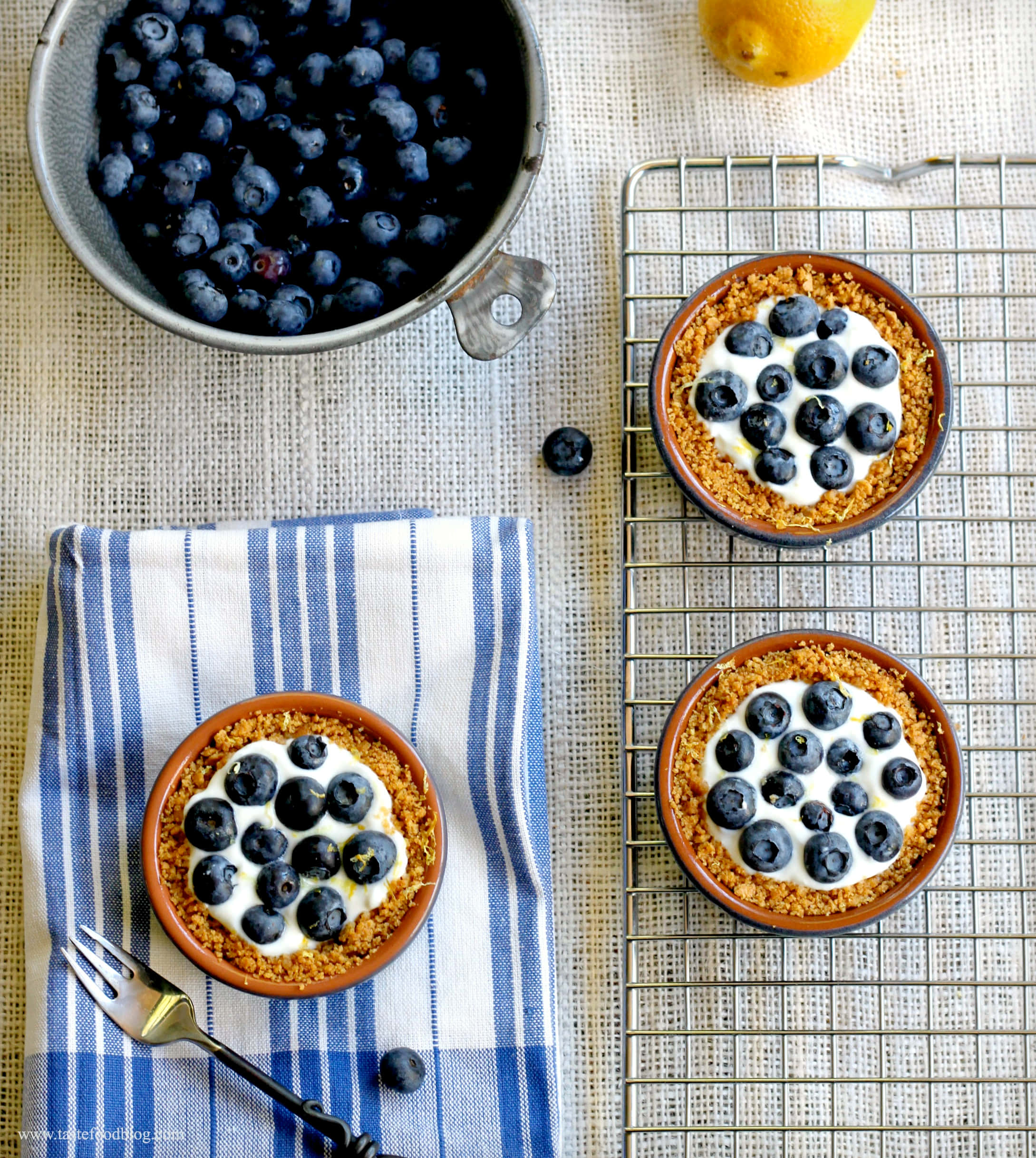 Blueberries Tart 桌布 壁紙 — 三個藍莓優格塔放在冷卻架上和條紋布上，旁邊有一碗新鮮莓果和檸檬。