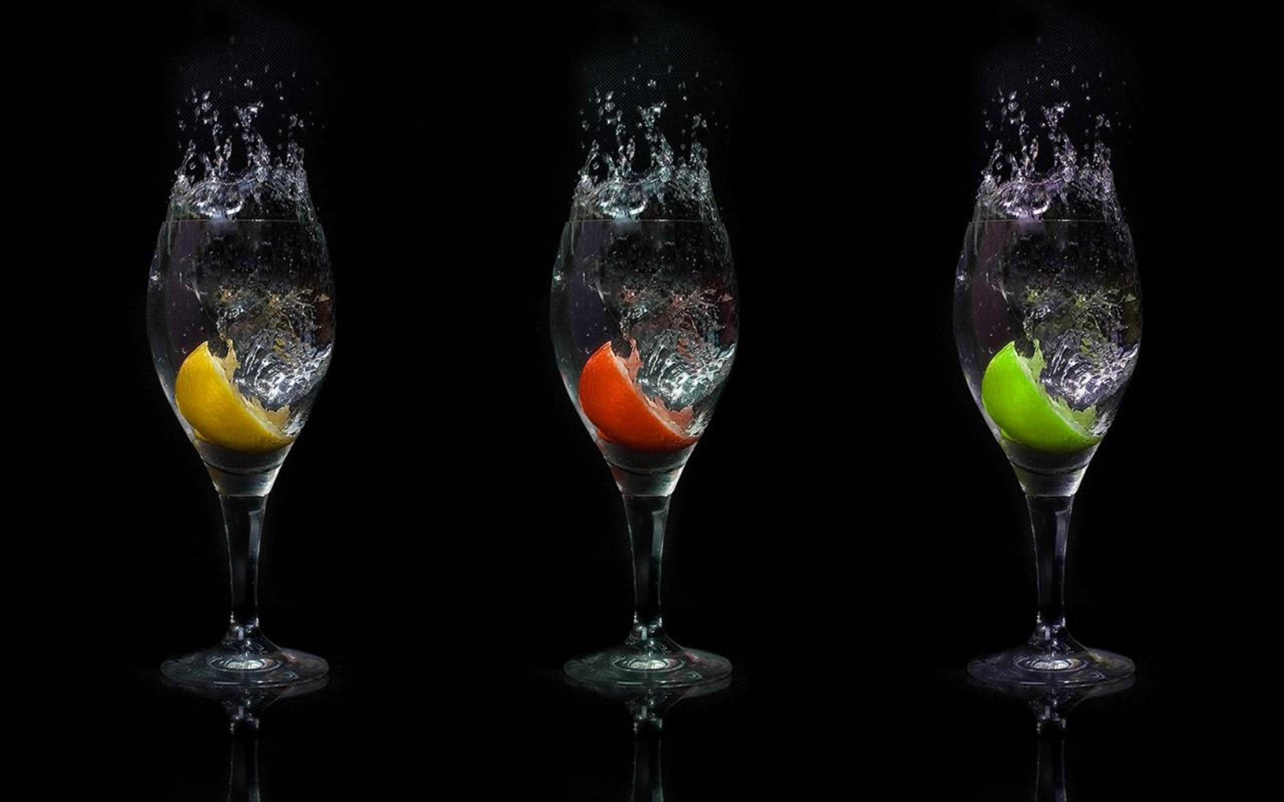 Drink 桌布 壁紙 — 三個裝滿水的酒杯展示充滿活力的柑橘片——黃檸檬、紅橙和青檸——在黑色背景上產生爆炸性的水花。