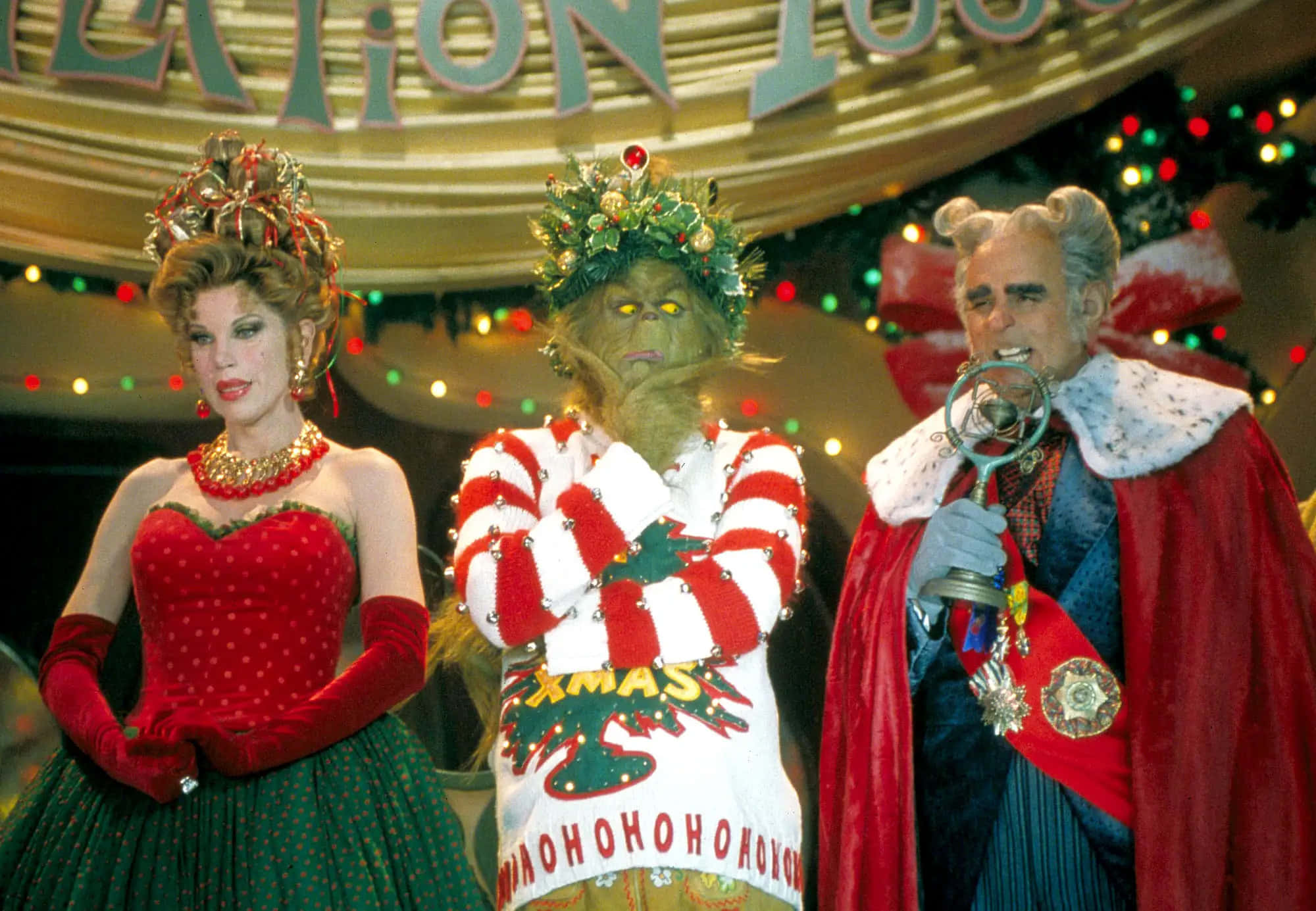 The Grinch 桌布 壁紙 — 三個角色穿著節日服裝，站在裝飾有閃爍燈光的拱門下。