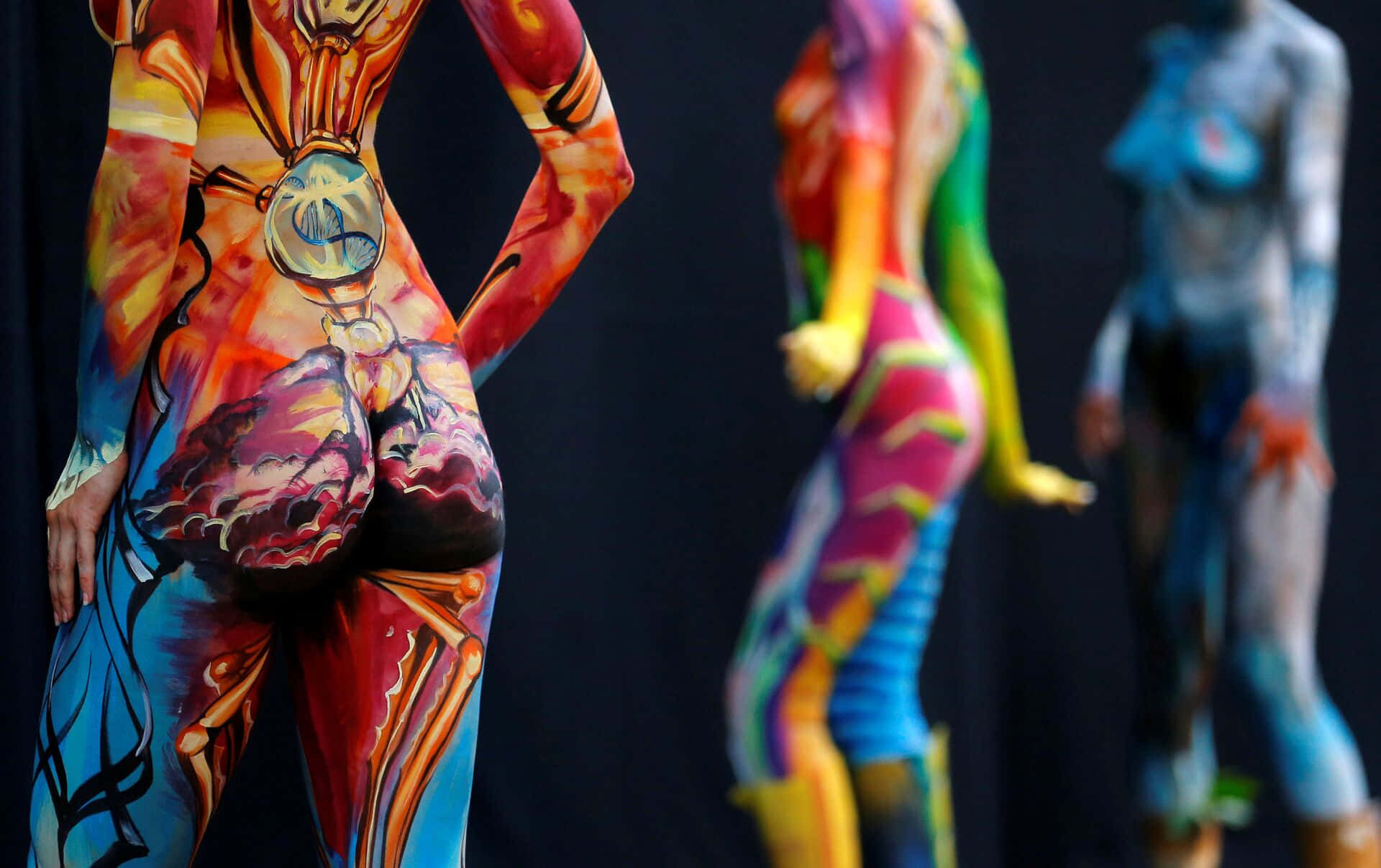 Body Painting Festival 桌布 壁紙 — 三個身上有鮮豔人體彩繪的人物站在深色背景前，展示複雜多彩的設計。