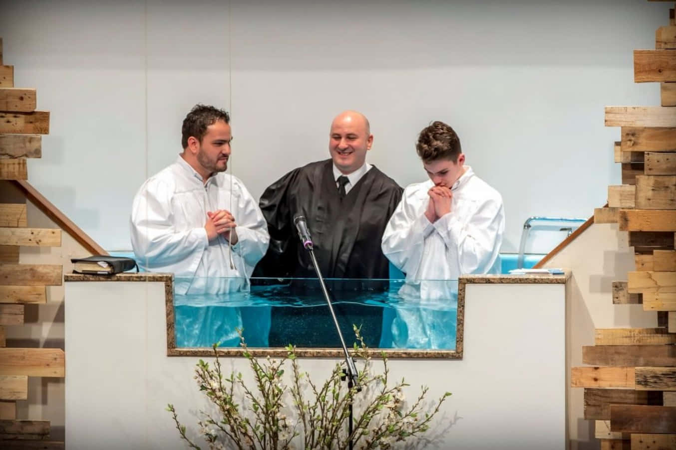 Baptism 桌布 壁紙 — 三個身穿白袍和一個身穿黑袍的男人站在一個有清澈藍色水的洗禮池旁，一個年輕男子正準備接受浸禮。