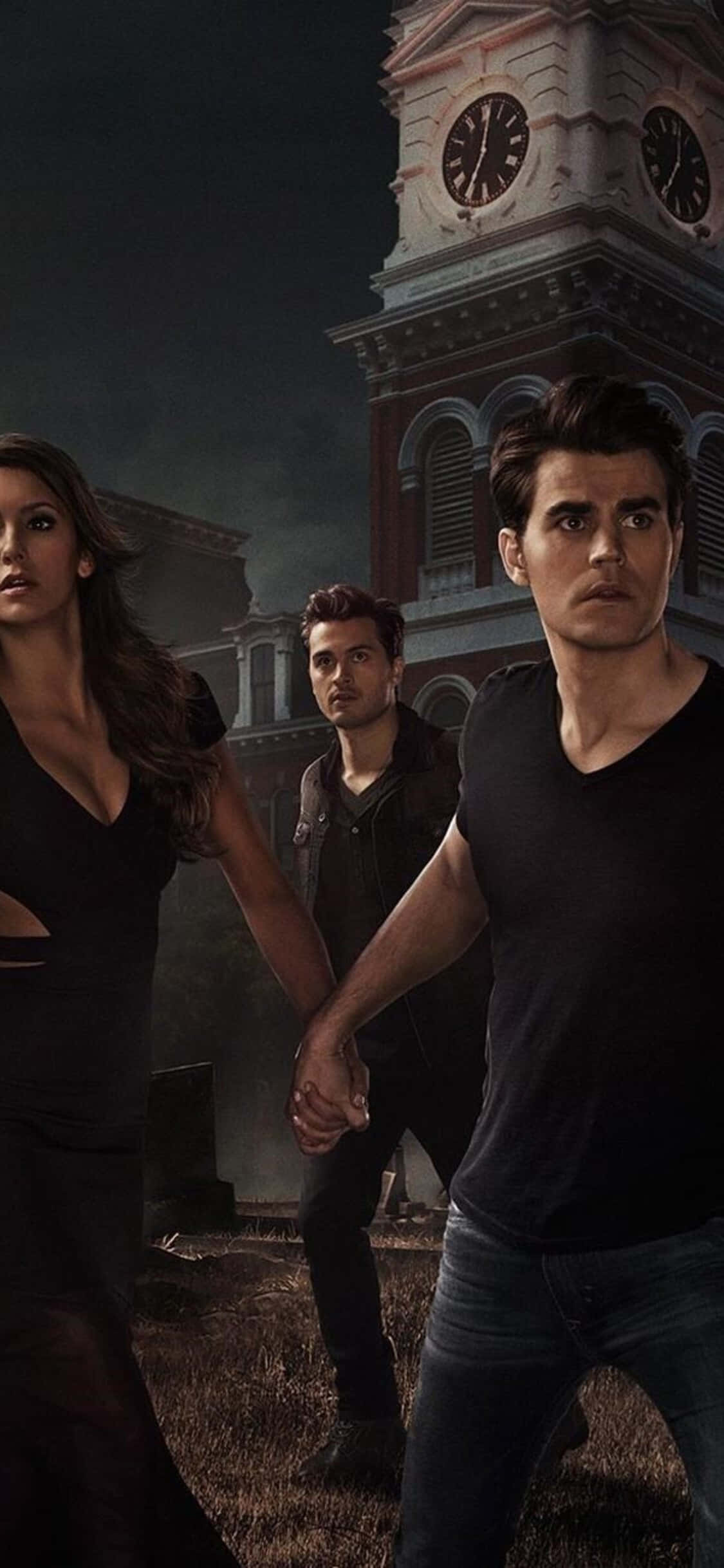 The Vampire Diaries iPhone 桌布 壁紙 — 三個身穿黑色的人物緊張地站在一座迫近的鐘樓前，背景是黑暗風暴的天空。