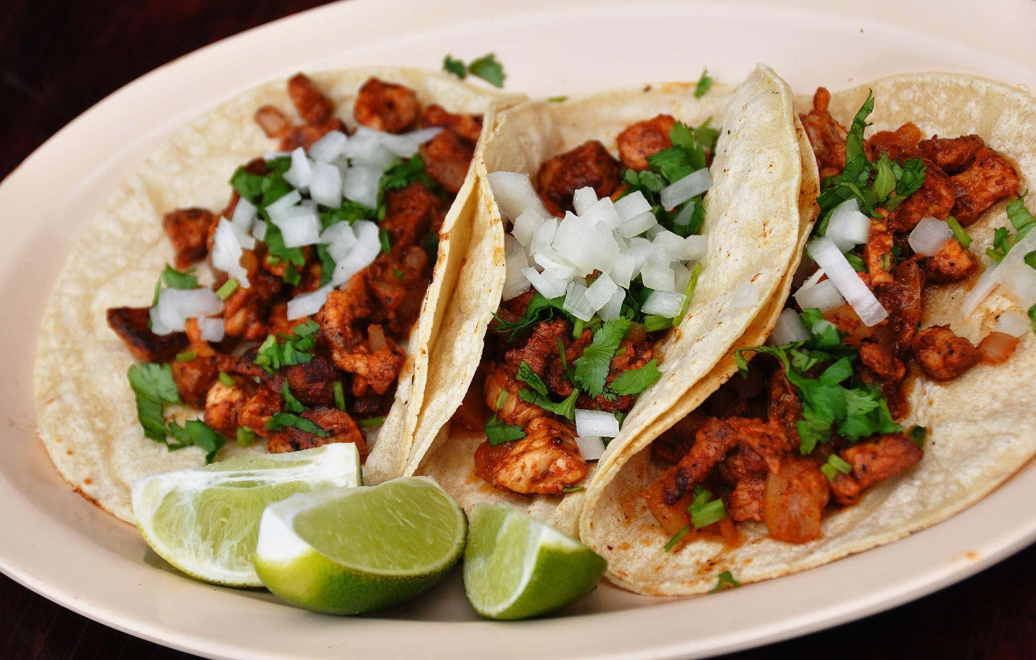 Taco 桌布 壁紙 — 三個軟玉米餅，內餡為調味肉、香菜和洋蔥，搭配萊姆角，盛於白盤中。