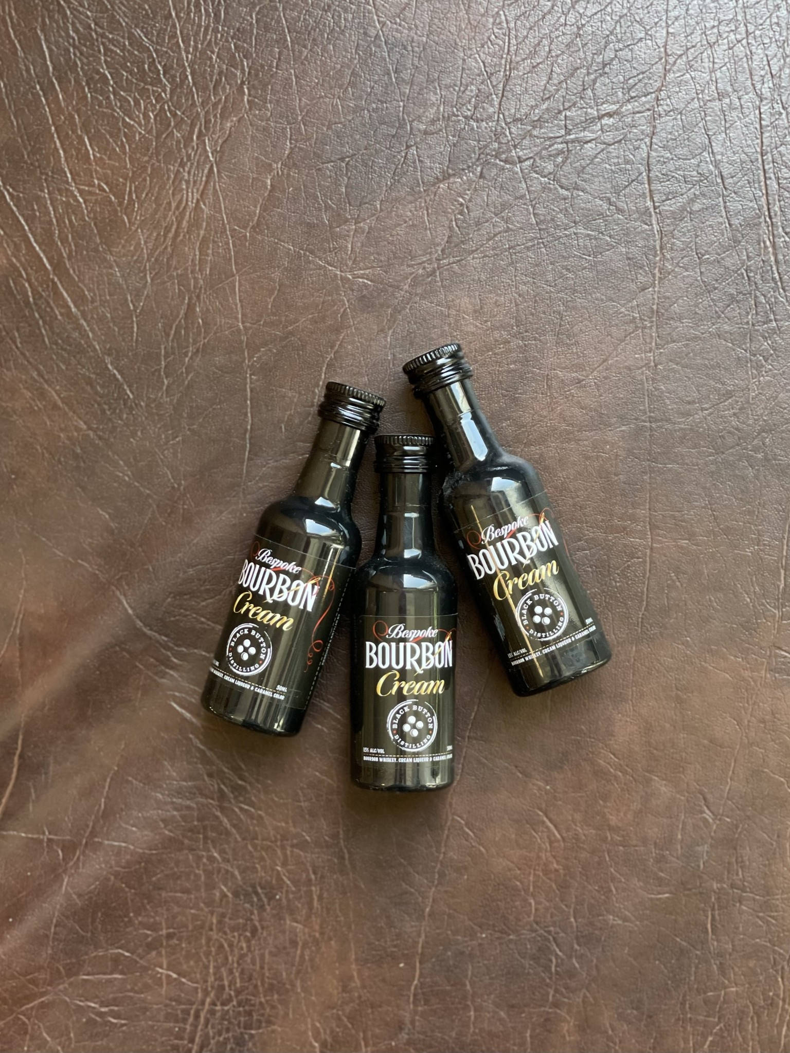 small 桌布 壁紙 — 三個迷你波本奶油酒瓶放在有紋理的棕色皮革表面上。