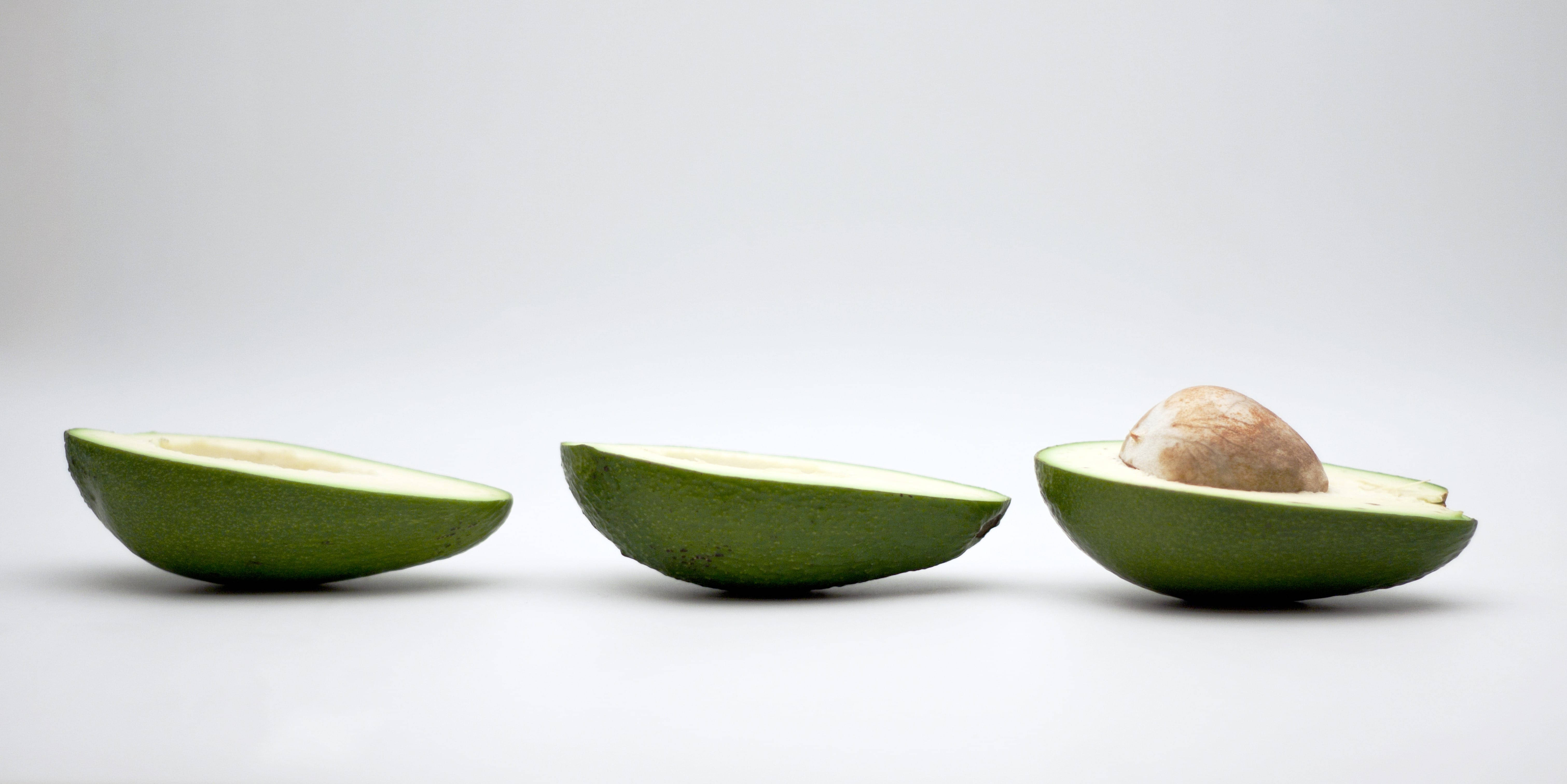 Fruits 桌布 壁紙 — 三個酪梨半邊排成一列放在白色背景上，其中一個帶有果核。