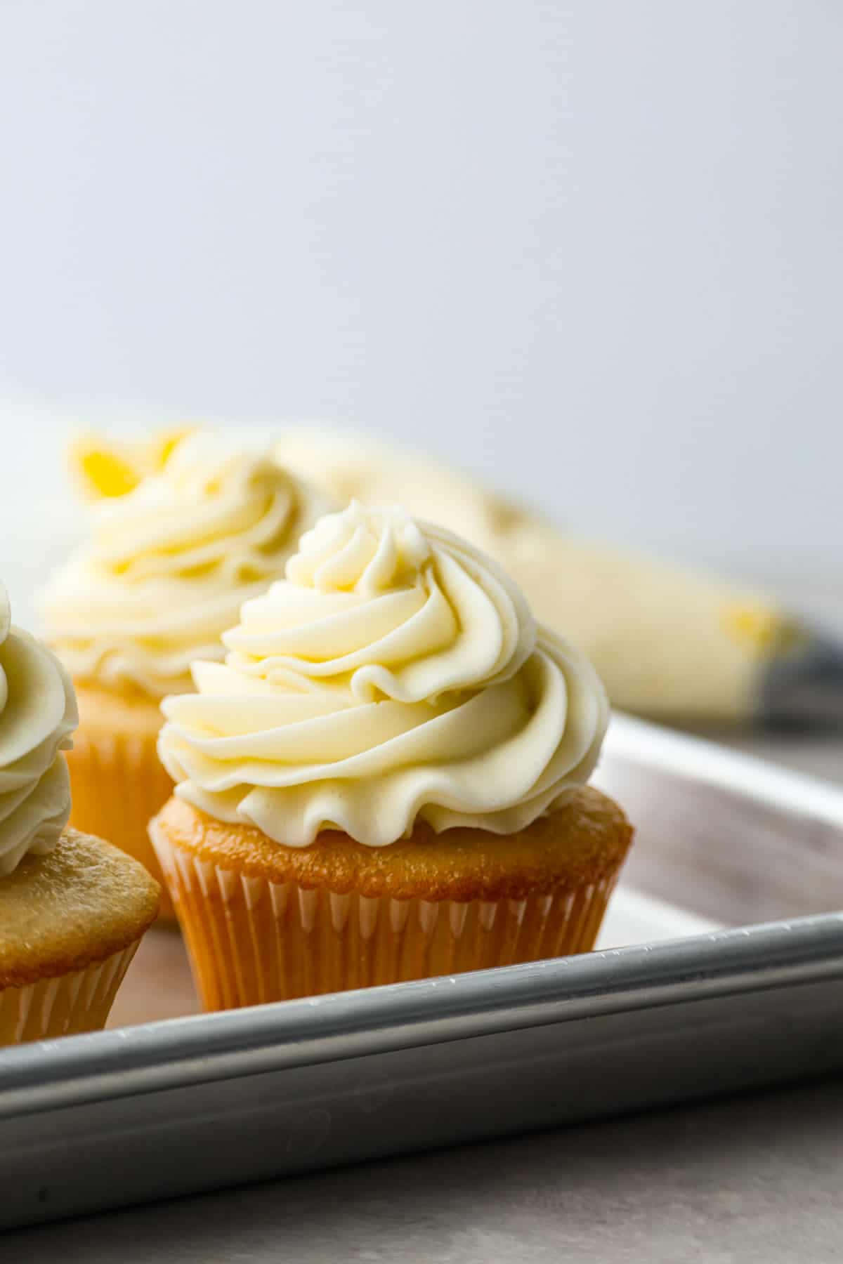 Buttercream 桌布 壁紙 — 三個金色杯子蛋糕，上面有奶油香草糖霜漩渦，放在金屬烤盤上。