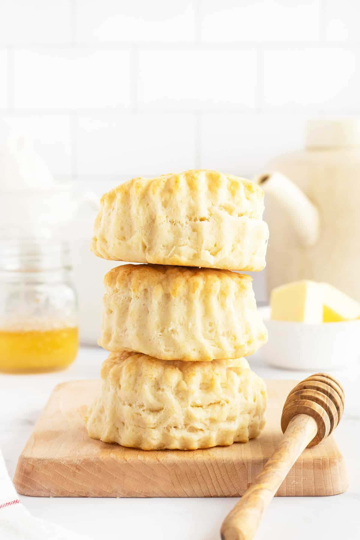 Biscuit 桌布 壁紙 — 三個金黃色的白脫牛奶餅乾堆疊在木板上，附近有蜂蜜蘸棒和奶油。