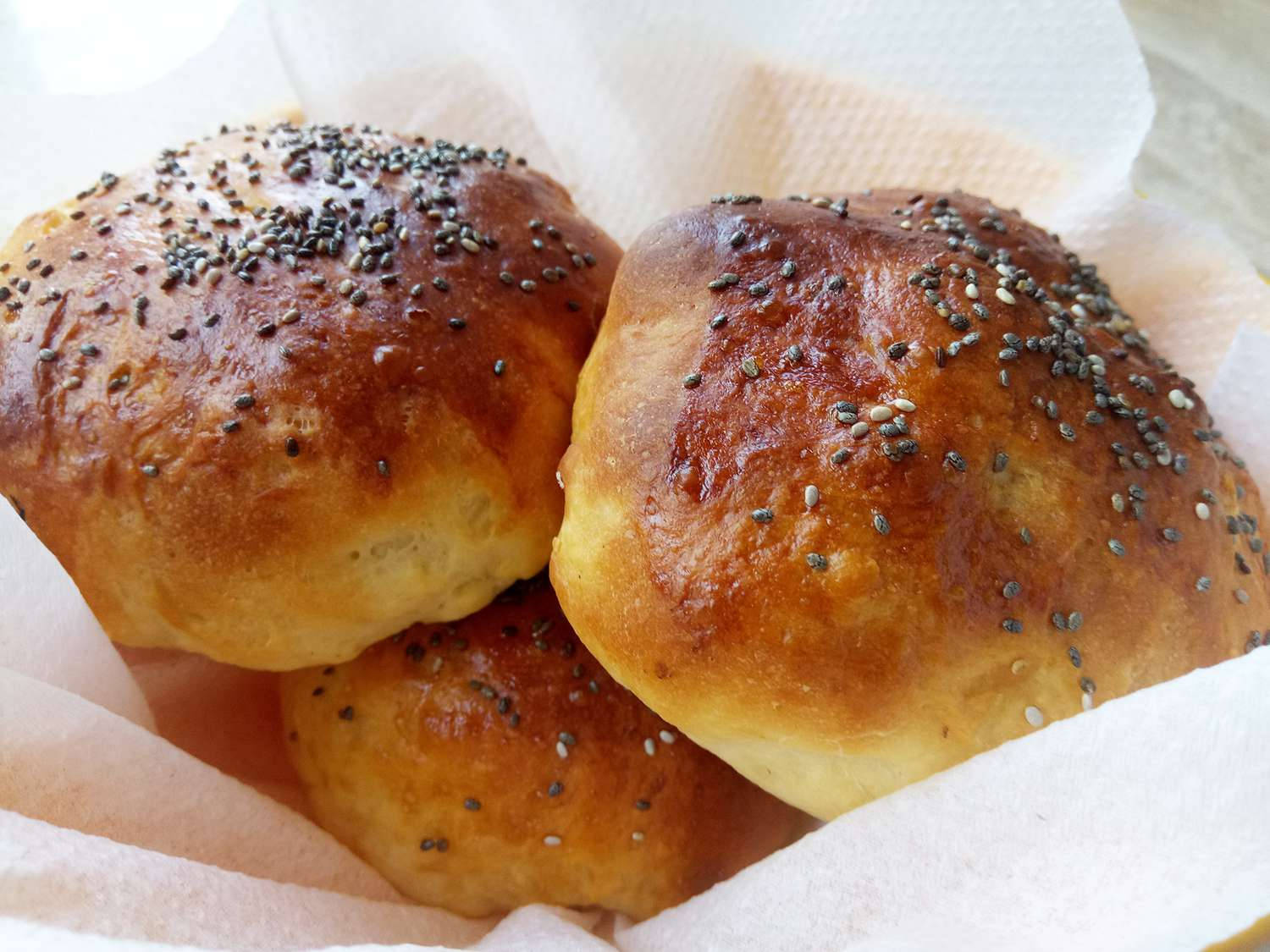 Pastry 桌布 壁紙 — 三個金黃色的種子麵包捲放在白色烘焙紙上，外皮閃閃發光。
