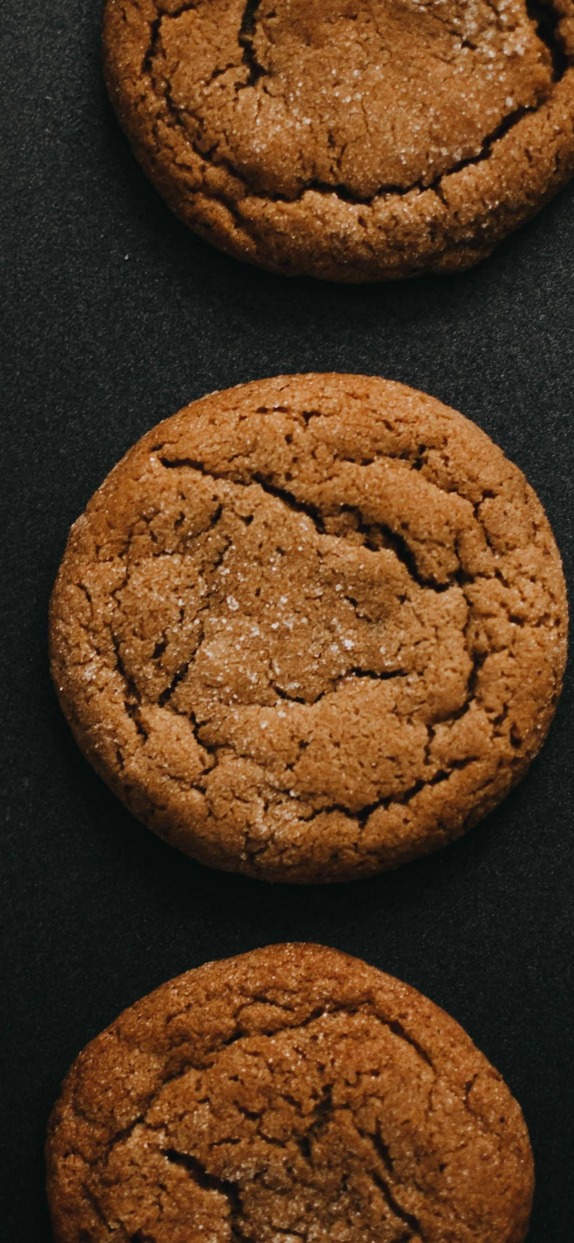 Cookie 桌布 壁紙 — 三個金黃色的糖餅乾，頂部有裂紋並灑上閃閃發光的糖，放在深色霧面表面上。