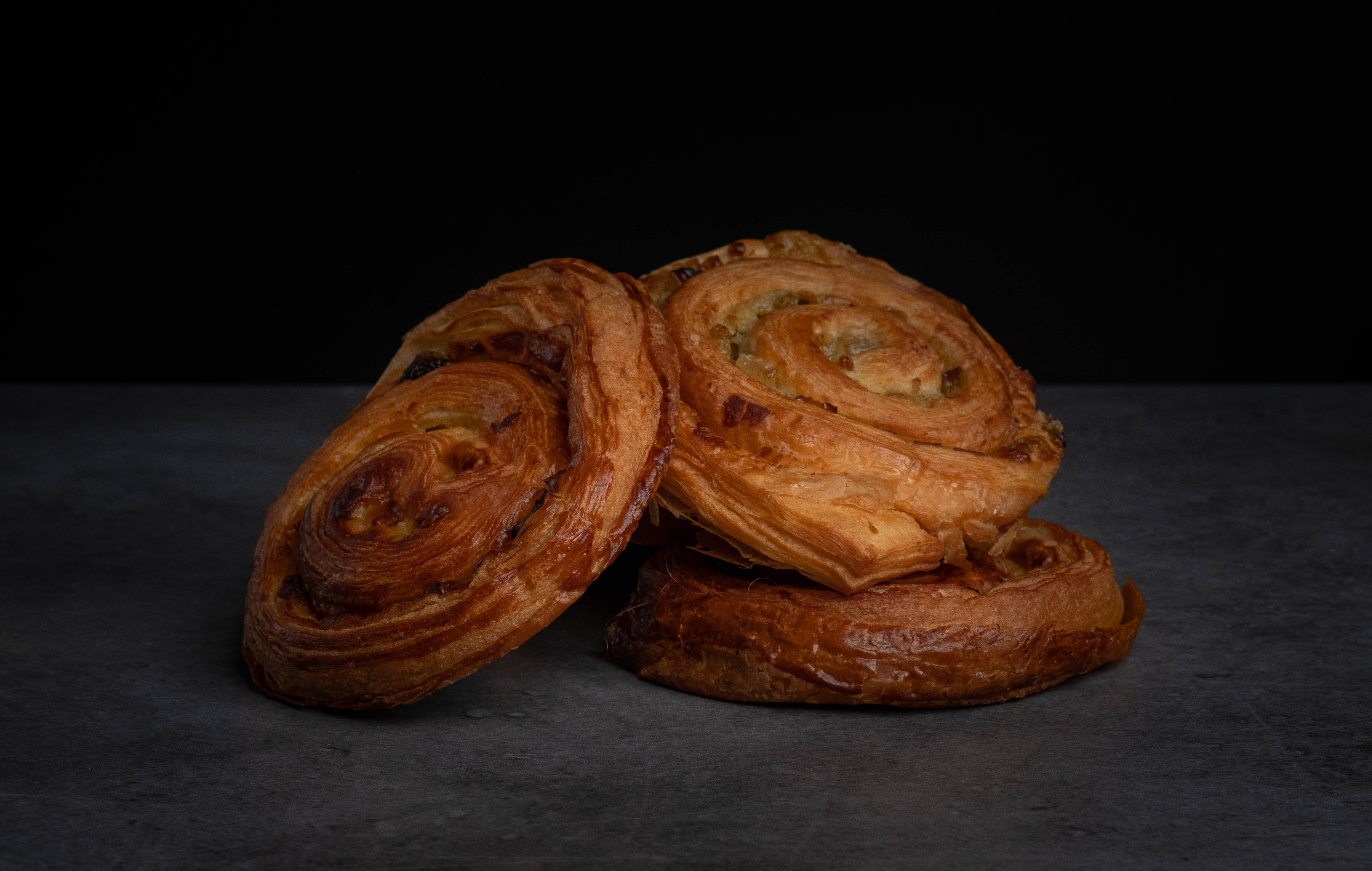Pastry 桌布 壁紙 — 三個金黃色螺旋狀酥皮糕點放在黑色背景的深灰色表面上。