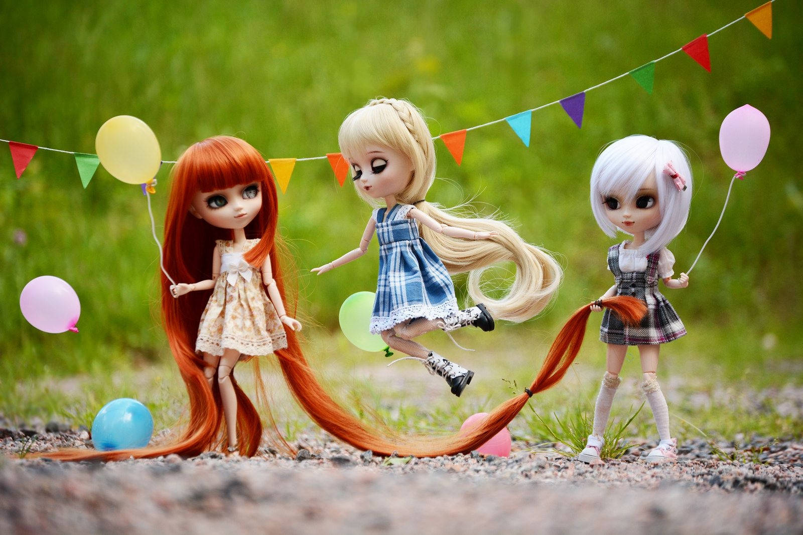 3 Best Friends 桌布 壁紙 — 三個長髮娃娃拿著氣球，在草地上色彩繽紛的三角旗幟下頑皮地擺姿勢。