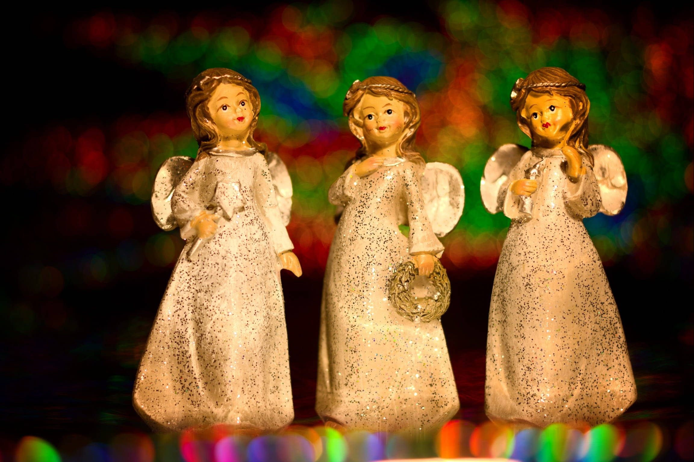 angels 桌布 壁紙 — 三個閃閃發光的天使雕像排成一排，背景是色彩繽紛的散景燈光。