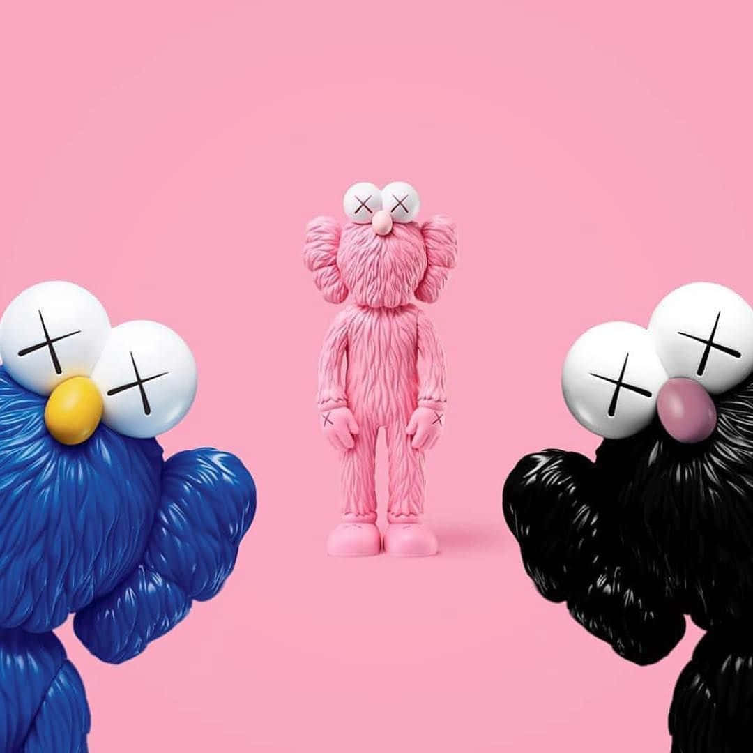 Kaws Bff Pink 桌布 壁紙 — 三個風格化的KAWS公仔，分別為粉紅色、藍色和黑色，站在純粉紅色背景上，帶有交叉的眼窩。