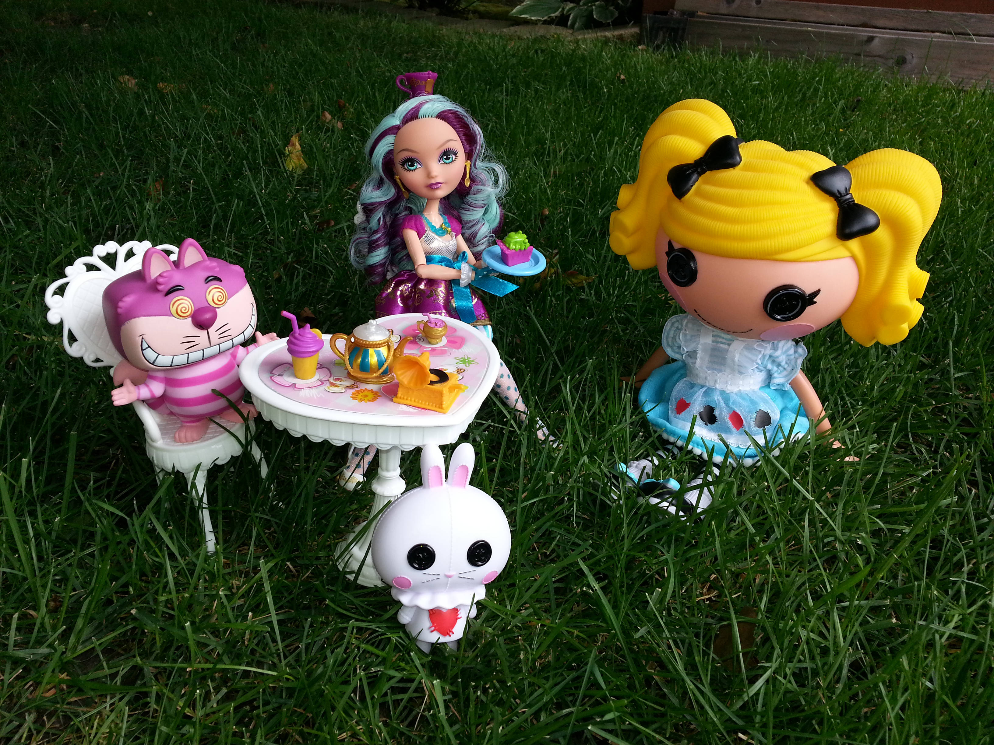 bratz 美學 桌布 壁紙 — 三個風格化的玩具公仔和一個貓公仔聚集在一個微型茶具周圍，背景是充滿活力的綠色草地。