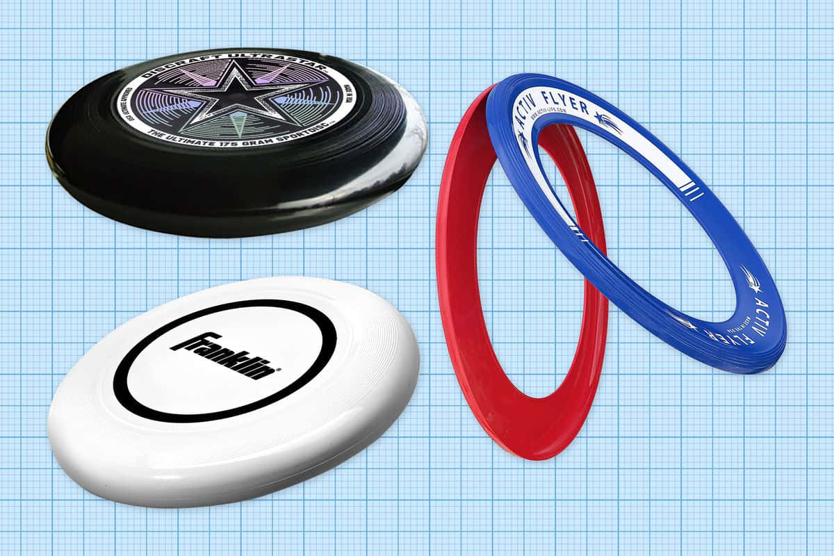 Disc Golf 桌布 壁紙 — 三個飛盤和兩個圓環，顏色有黑、白、紅、藍，放置在淺藍色網格背景上。