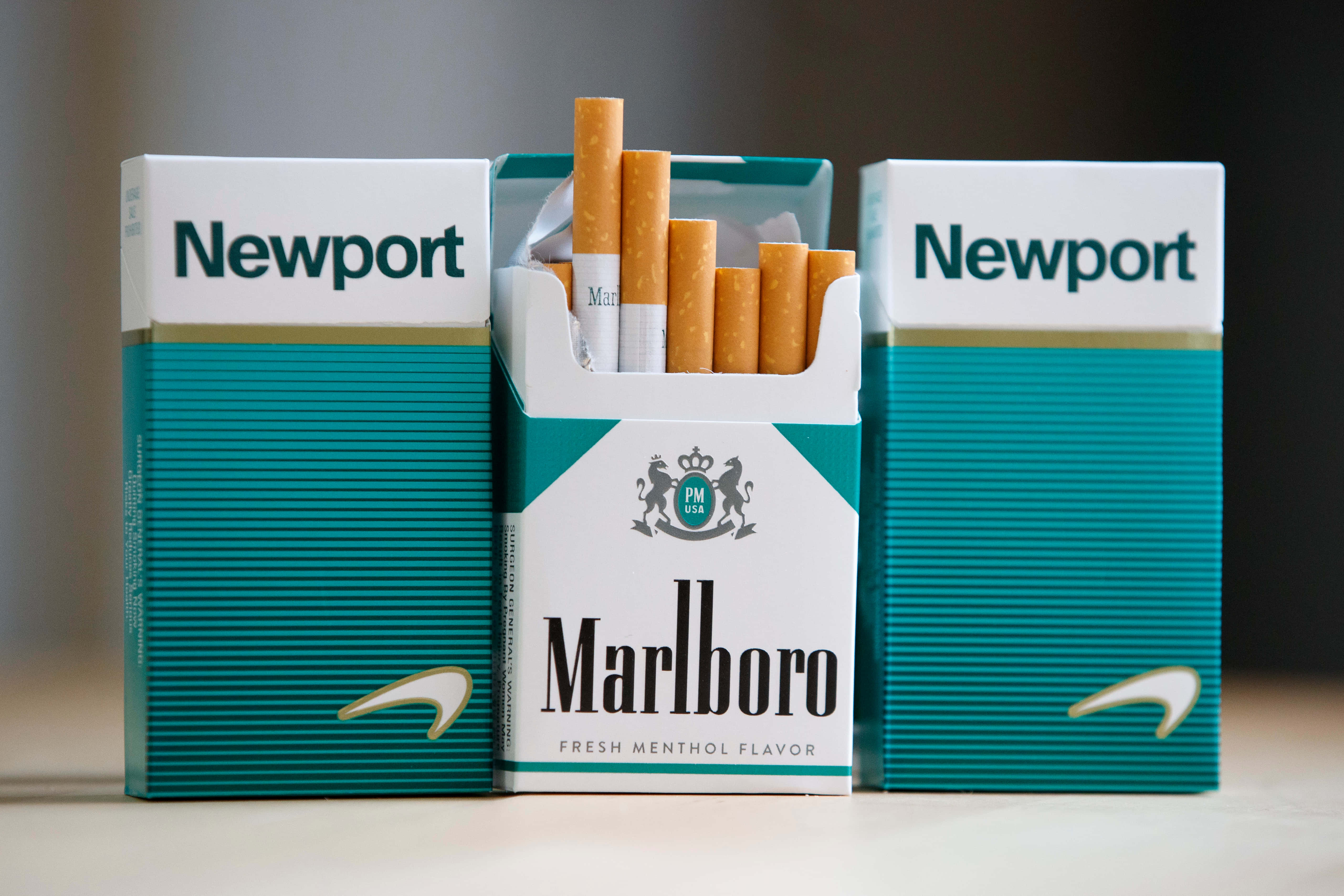cigarettes 桌布 壁紙 — 三個香煙包，包括一個萬寶路薄荷煙包，香煙散落在模糊的背景上。