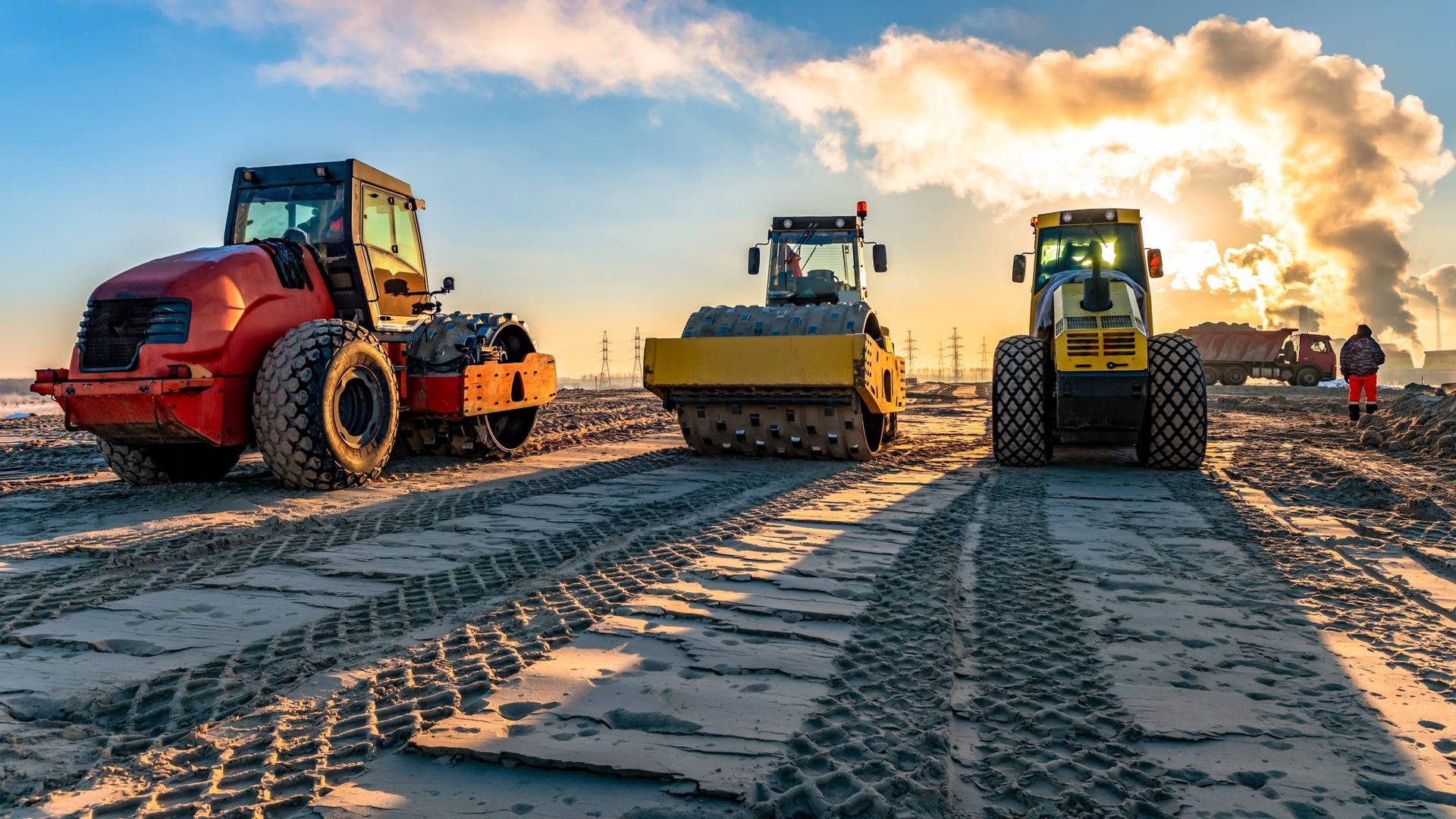 construction 桌布 壁紙 — 三台重型壓路機在金色日落時分，在廣闊泥濘的建築工地上留下深深的輪胎痕跡。