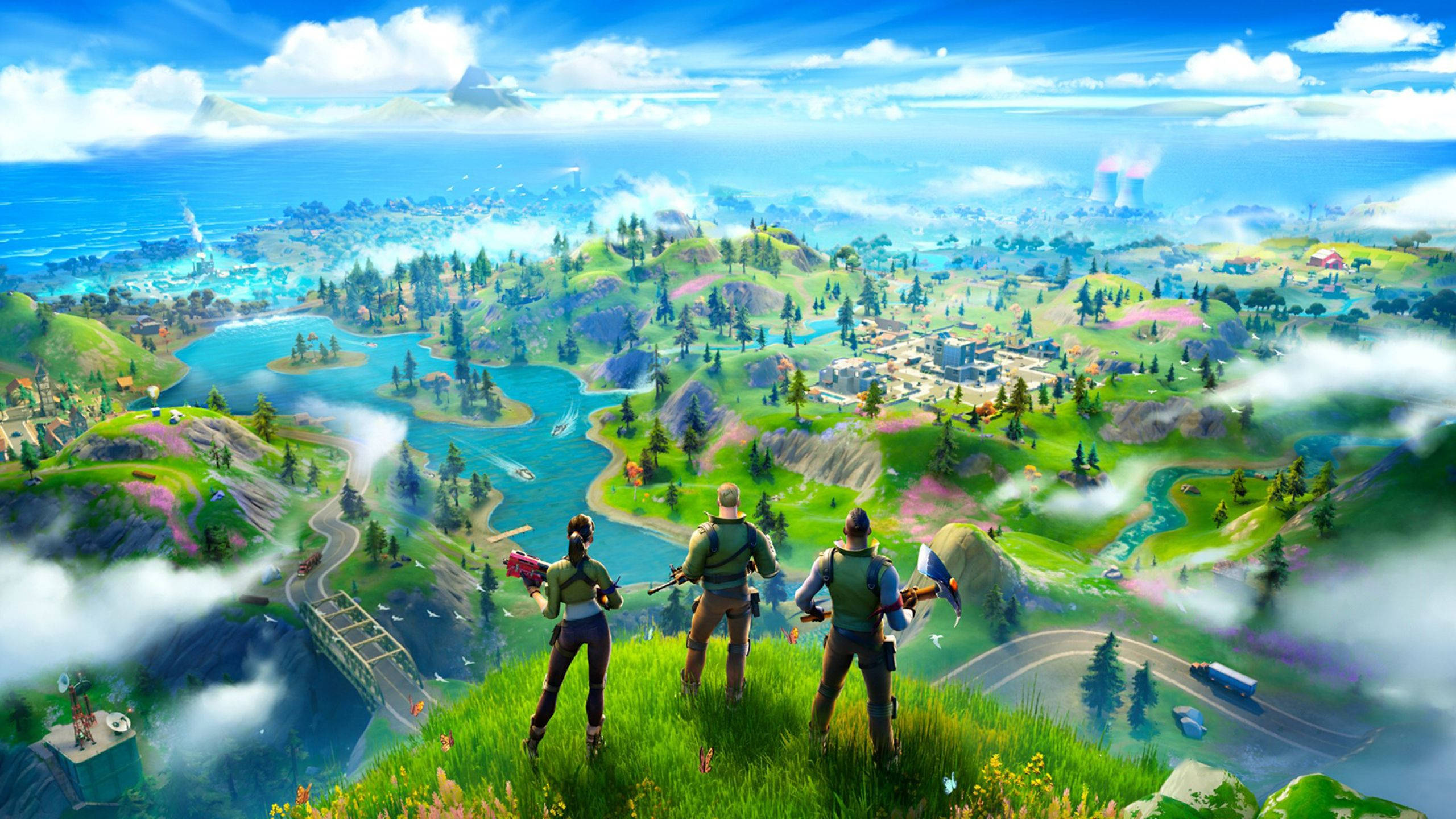Fortnite 桌布 壁紙 — 三名Fortnite玩家站在長滿青草的懸崖頂上，俯瞰著一個充滿活力的島嶼，島上有湖泊、森林和遠處的城鎮，天空湛藍明亮。