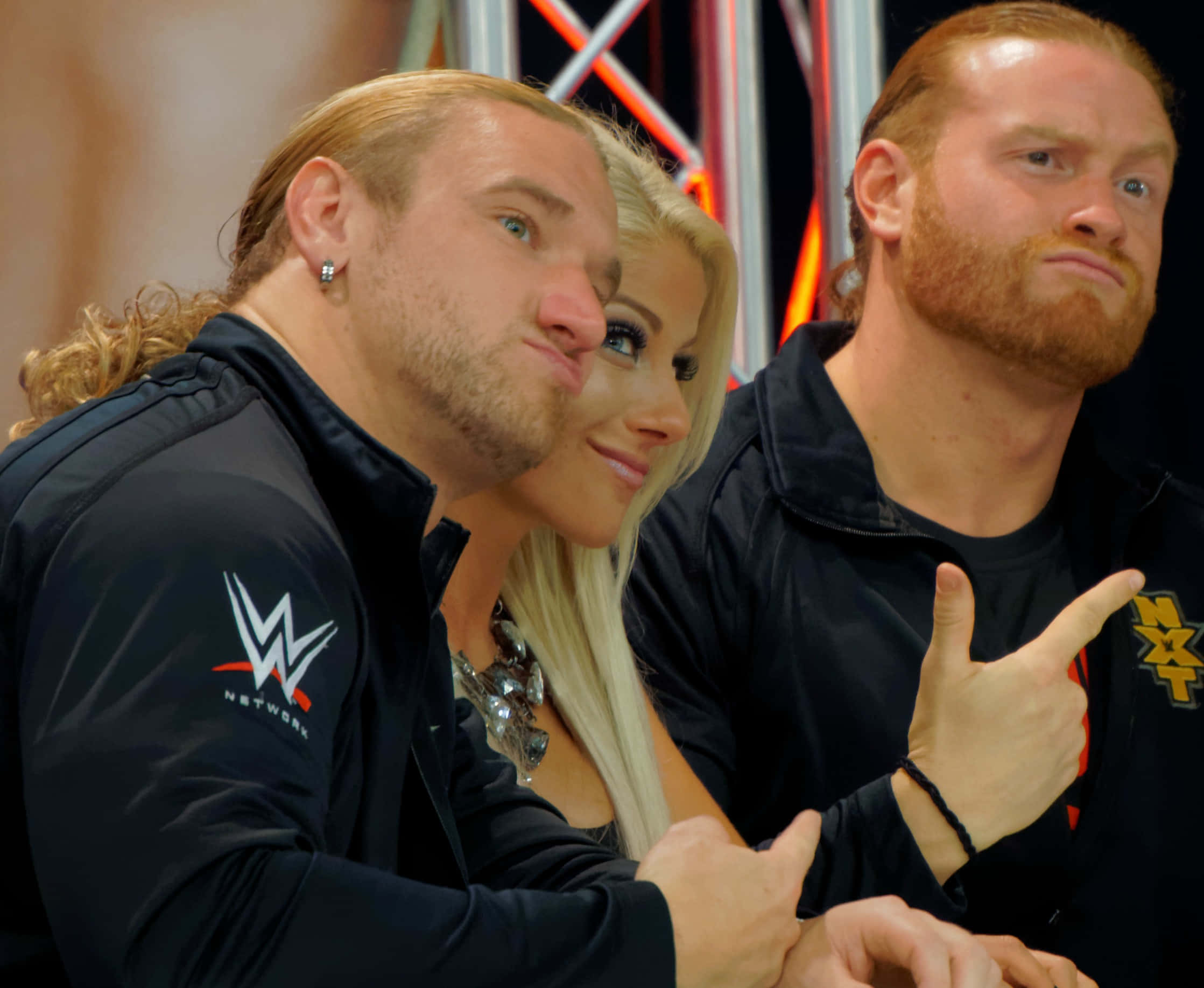 WWE 桌布 壁紙 — 三名WWE摔角手與一名身穿黑色外套的女子在摔角活動中自信地一起擺姿勢。