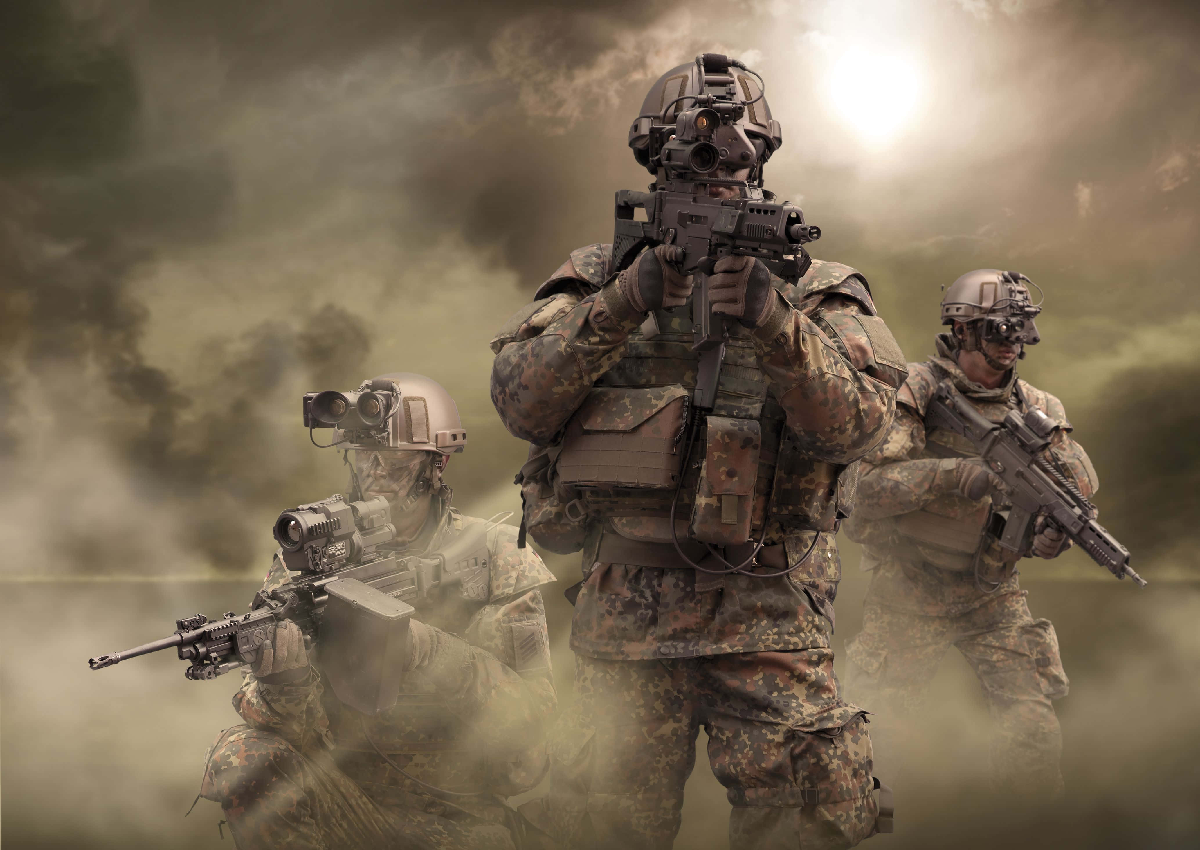 軍隊 桌布 壁紙 — 三名全副武裝的士兵在煙霧瀰漫的戰場上，在明亮的陽光下保持警覺。