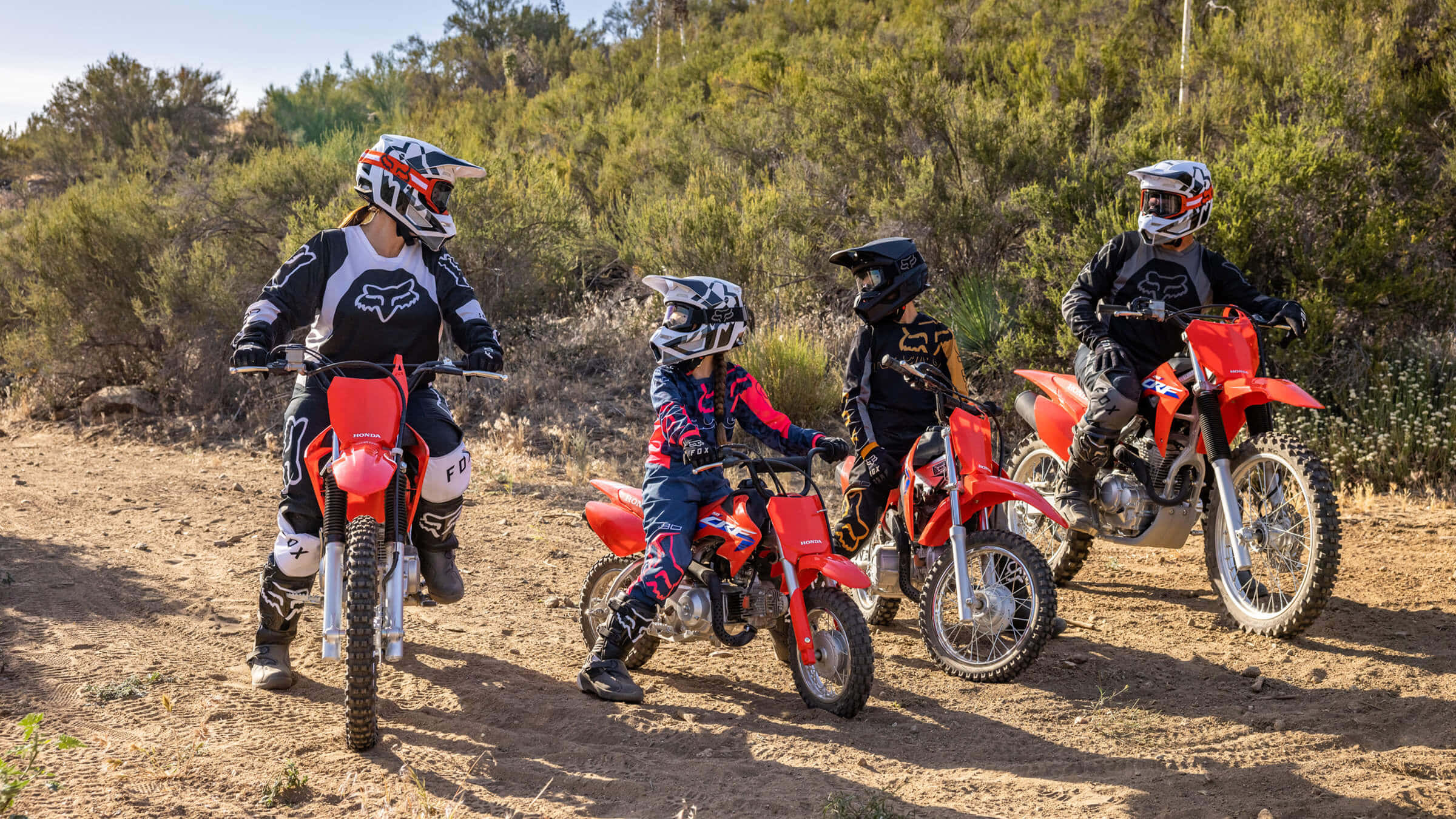 Dirtbike 桌布 壁紙 — 三名全副裝備的騎士在明亮的日光下，在乾燥的灌木叢中停在紅色越野車上。