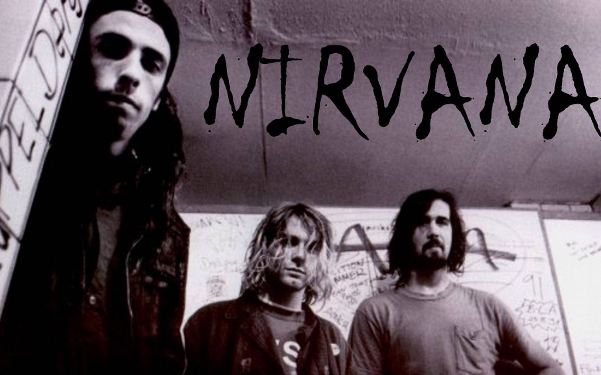 nirvana 4K 桌布 壁紙 — 三名垃圾搖滾樂團成員在佈滿塗鴉的牆前，頭頂有粗體黑色字母「NIRVANA」，他們凝視著鏡頭。