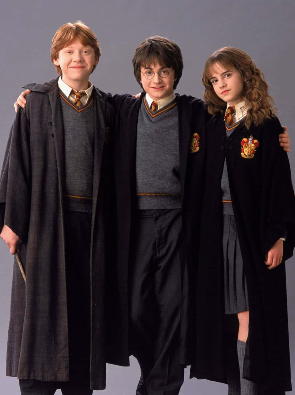 Ron Weasley 桌布 壁紙 — 三名年輕巫師穿著霍格華茲制服，在純灰色背景前緊密地站在一起。