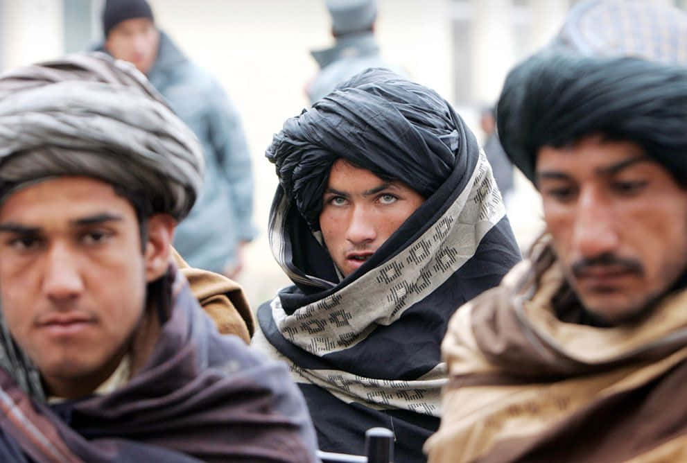 Taliban 桌布 壁紙 — 三名戴著傳統頭巾的男子在擁擠的街景中專注地向前凝視。