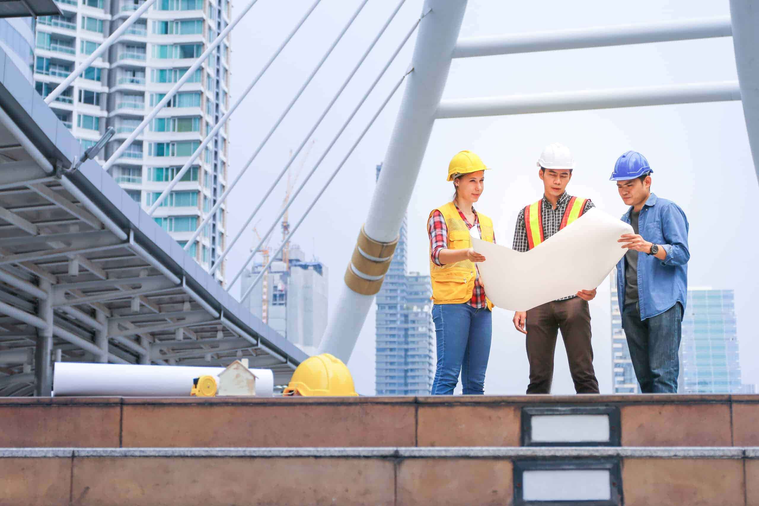 engineering 桌布 壁紙 — 三名戴著安全帽的建築工人在一座現代橋樑上審閱藍圖，背景是高樓大廈。