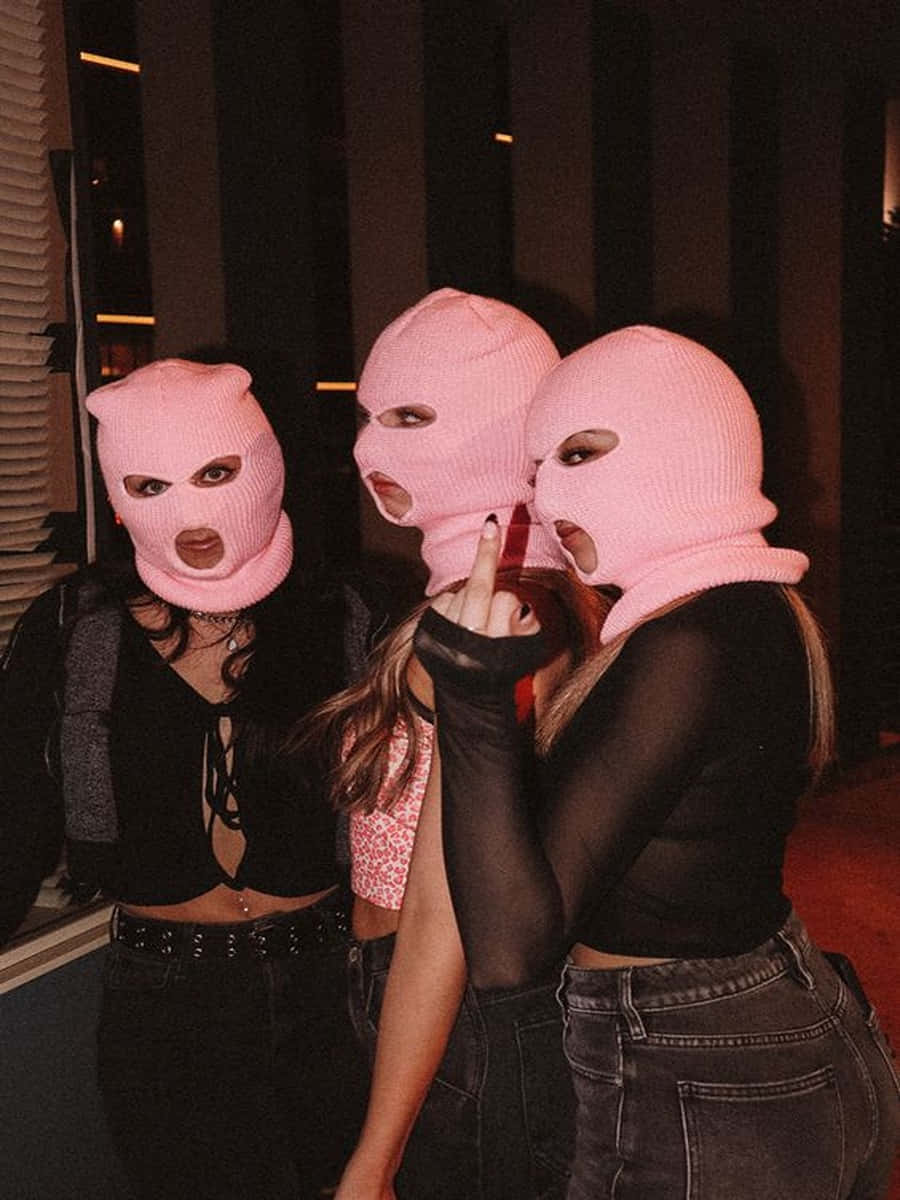 Ski Mask Girl 桌布 壁紙 — 三名戴著粉紅色巴拉克拉瓦頭套的女性在夜間挑釁地擺姿勢，其中一人豎起中指。