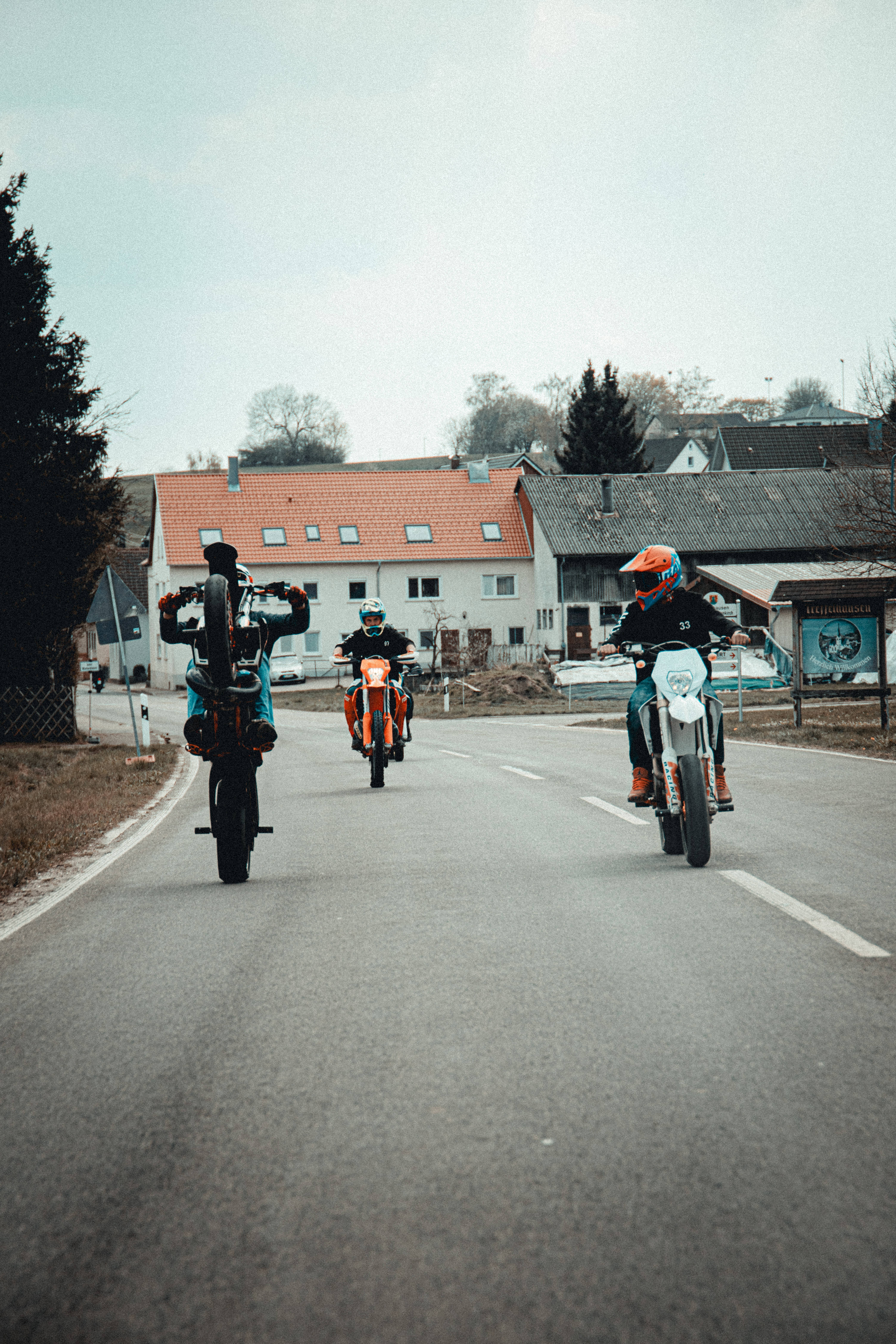 Ktm Bike 桌布 壁紙 — 三名摩托車手在陰天下行駛在鄉村道路上，經過房屋。