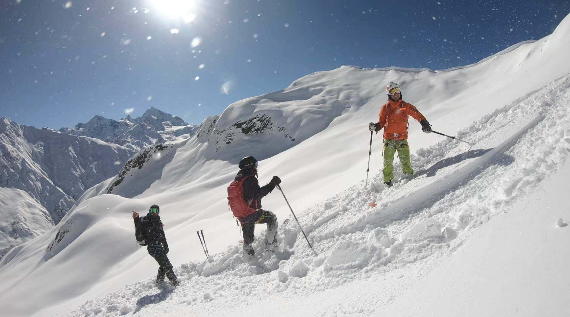滑雪 桌布 壁紙 — 三名滑雪者在晴朗藍天和太陽耀斑下，於明亮的雪山斜坡上滑行。