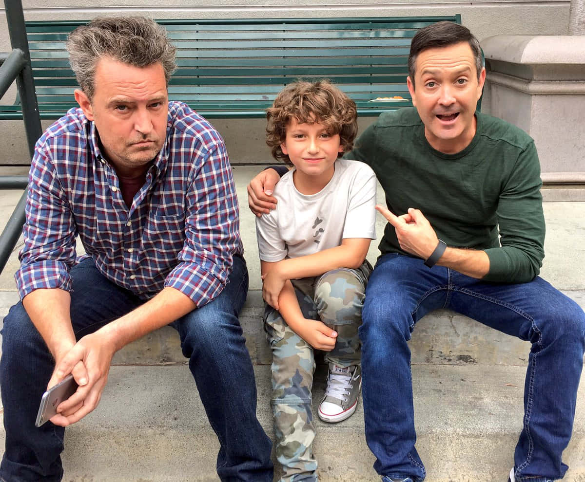 thomas lennon 桌布 壁紙 — 三名男子包括一名男孩坐在石階上，旁邊有一張綠色長椅，表情形成對比。
