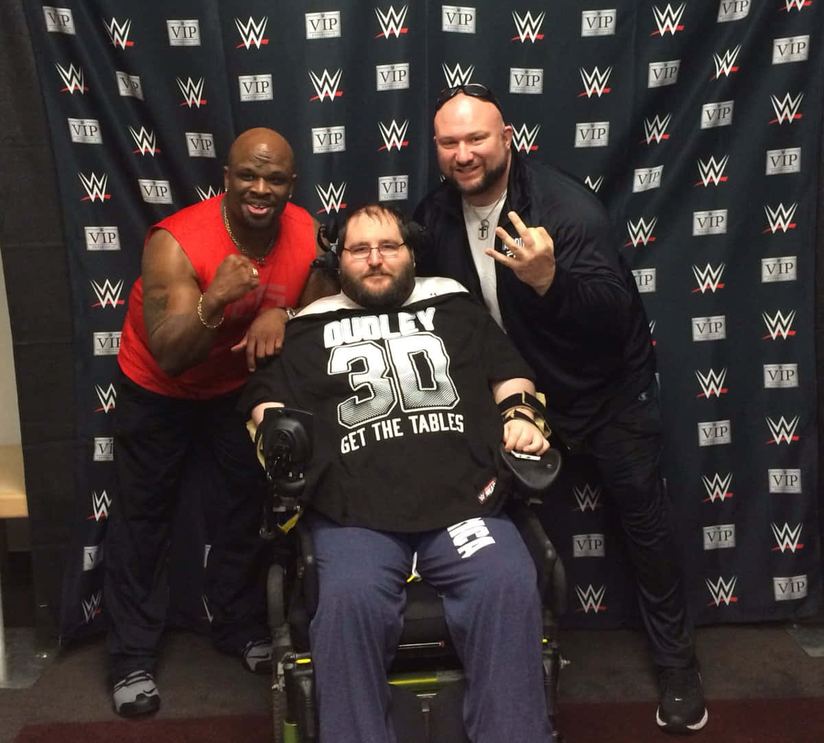 Wrestling 桌布 壁紙 — 三名男子在WWE VIP背景前愉快地擺姿勢，其中一人坐在輪椅上，身穿Dudley 30襯衫。
