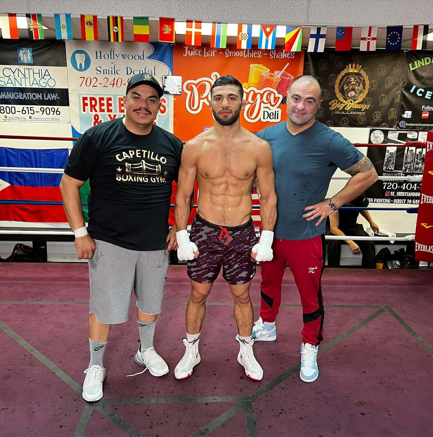 MMA 桌布 壁紙 — 三名男子在拳擊台上自信地擺姿勢，身後有旗幟和健身房橫幅。