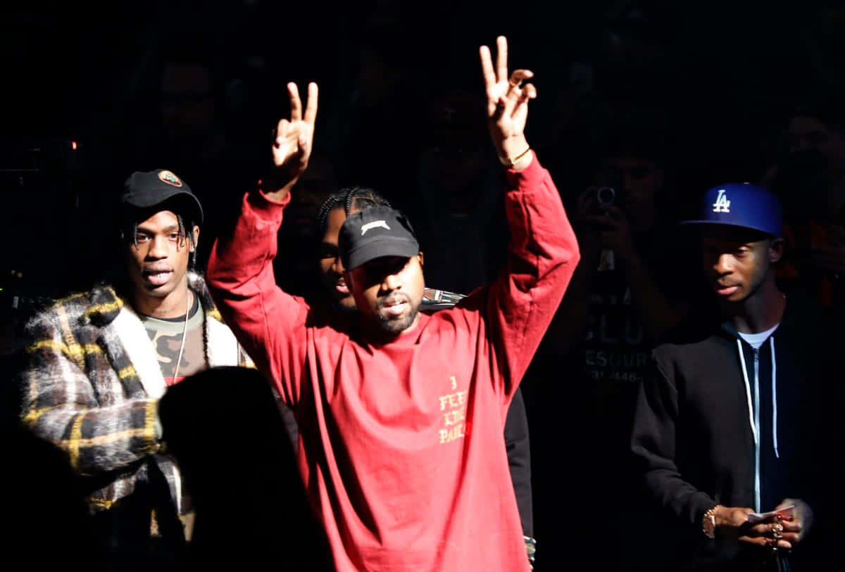 The Life Of Pablo 桌布 壁紙 — 三名男子在昏暗的演唱會燈光下舉起和平手勢，中間一人身穿紅衫黑帽。