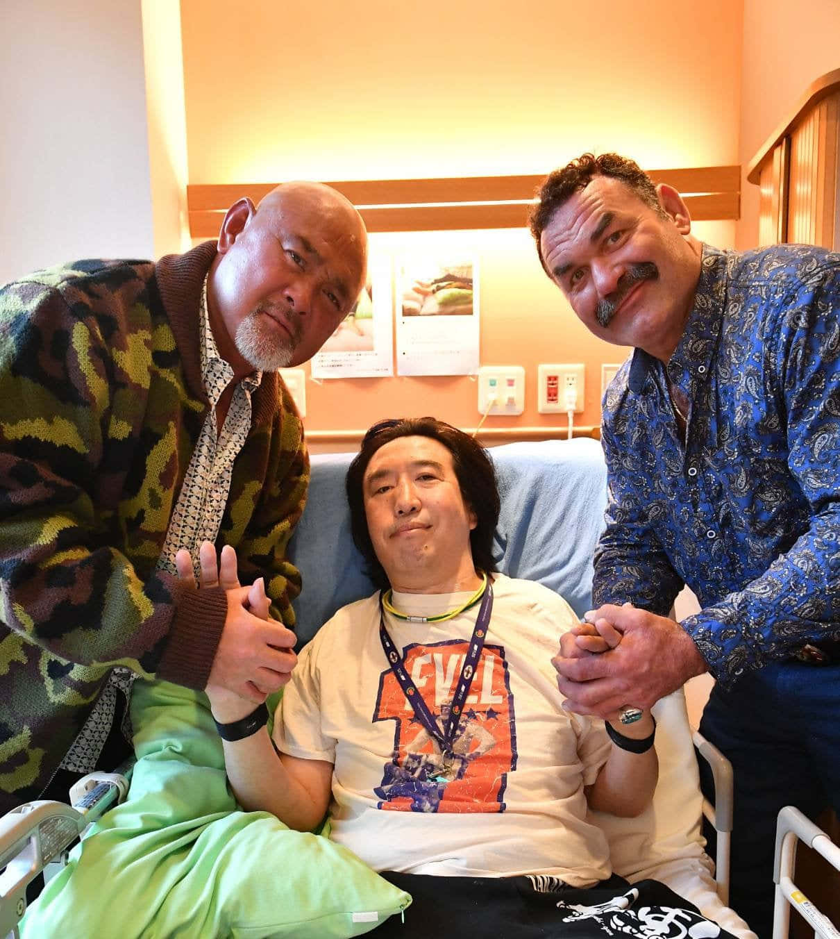Hospital 桌布 壁紙 — 三名男子在醫院病房內，兩人站在坐輪椅的男子兩側，溫暖地握著他的手。
