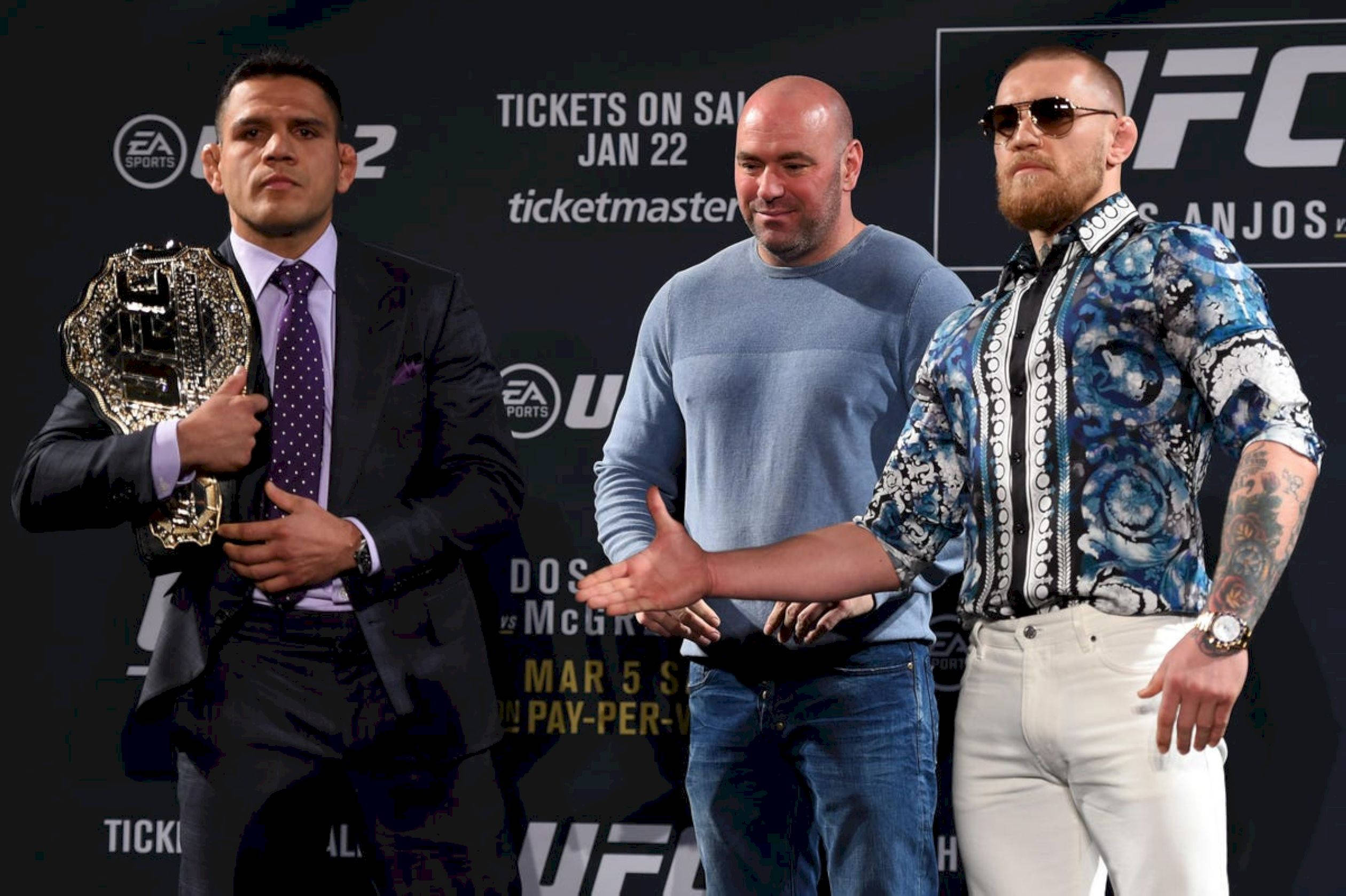 UFC 桌布 壁紙 — 三名男子站在UFC記者會上，一人手持冠軍腰帶，另一人戴著太陽眼鏡和穿著圖案襯衫。