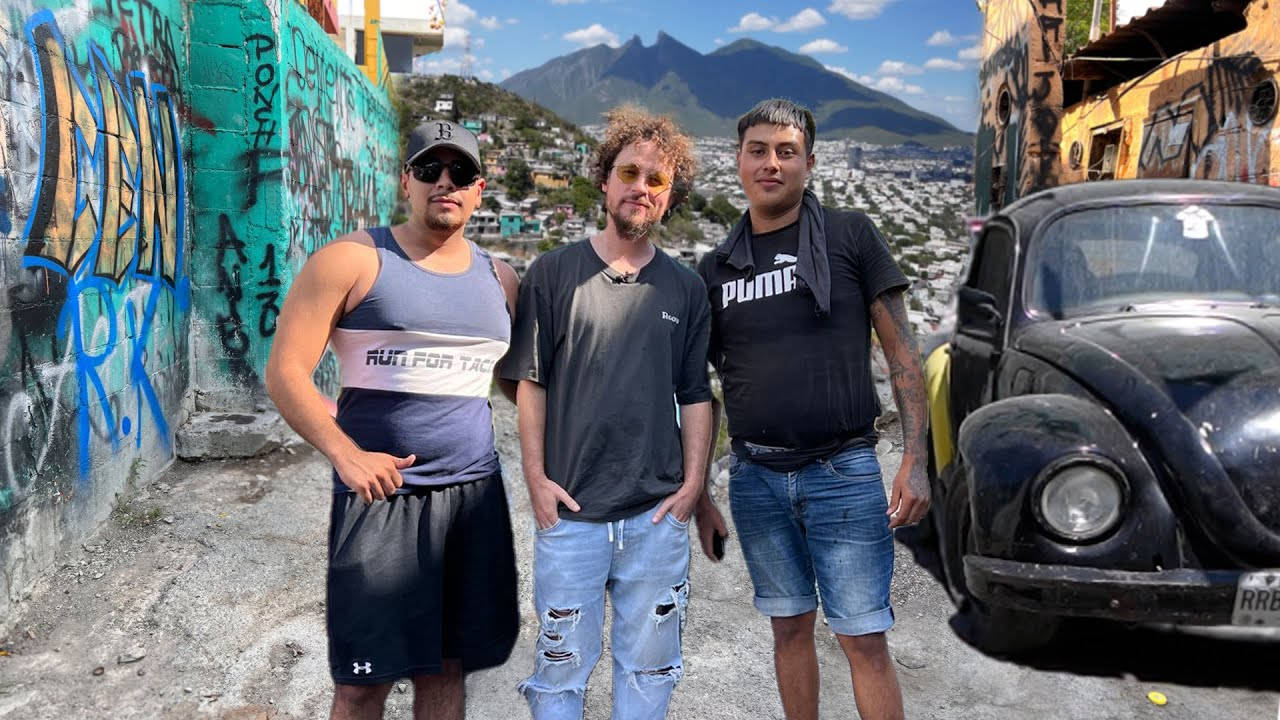 Black 桌布 壁紙 — 三名男子隨意地站在一輛復古黑色福斯金龜車旁邊，背景是佈滿塗鴉的牆壁和山巒城市景觀。